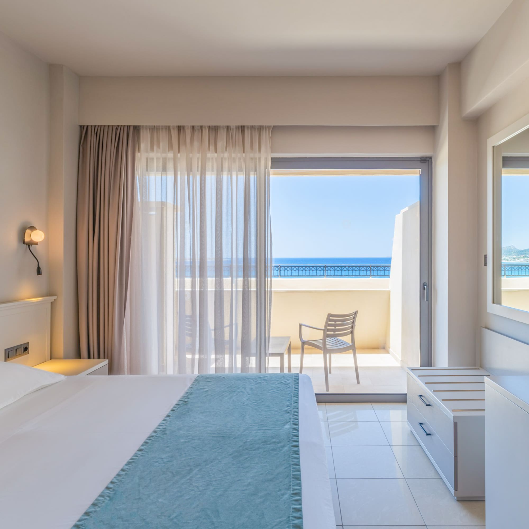 Bright hotel bedroom with sea view balcony and contemporary furnishings.