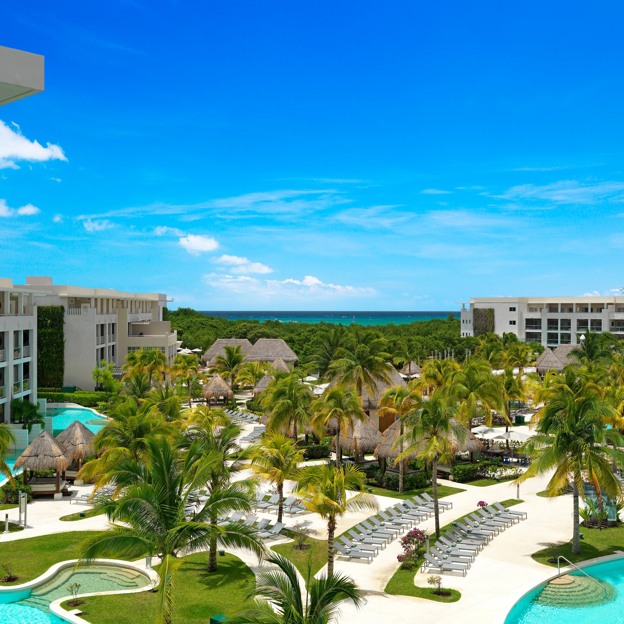 Luxury tropical resort with pools, palm trees, modern architecture, and ocean.
