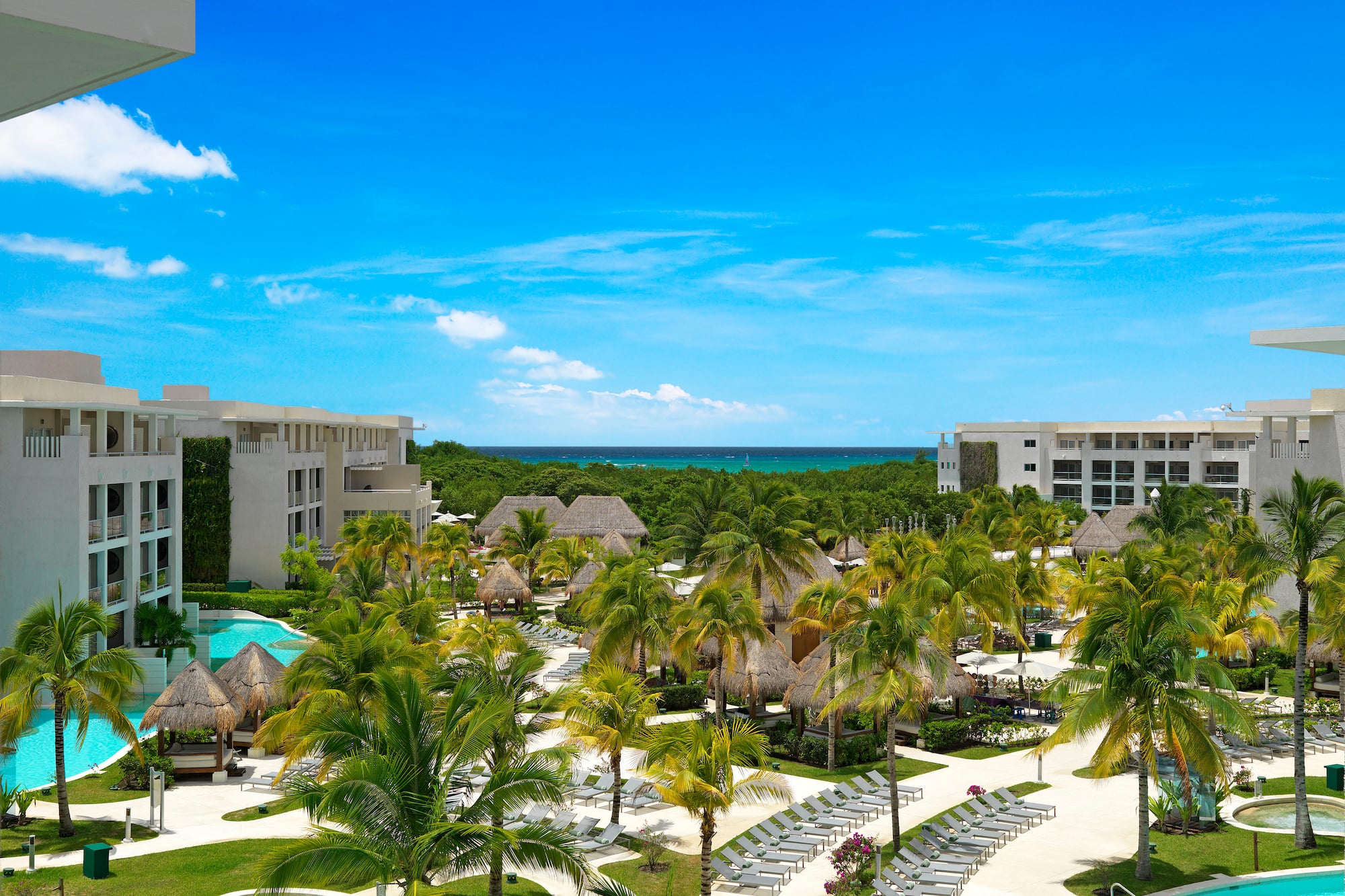 Tropical resort with pools, palm trees, and ocean view against blue sky.
