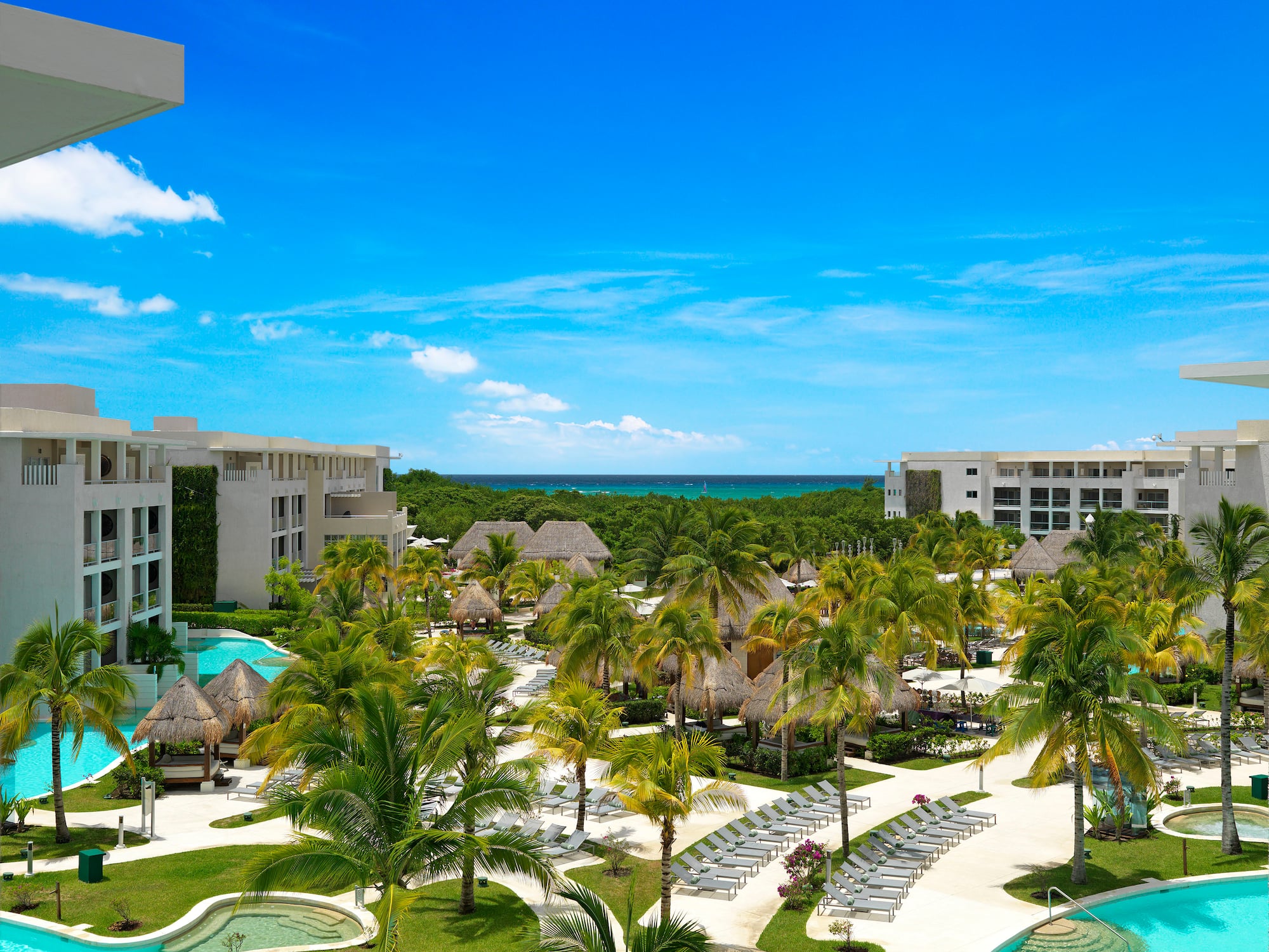 Luxury tropical resort with pools, palm trees, modern architecture, and ocean.