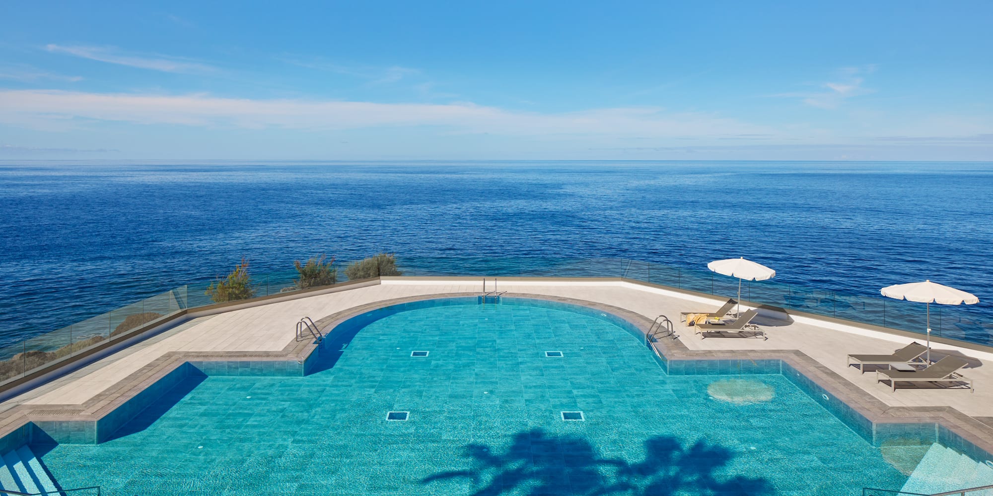 a swimming pool with a deck chair and umbrella overlooking the ocean