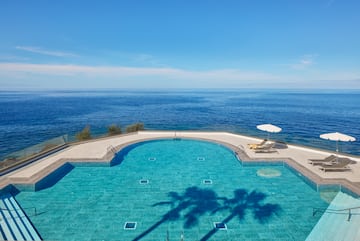 a swimming pool with a deck chair and umbrella overlooking the ocean