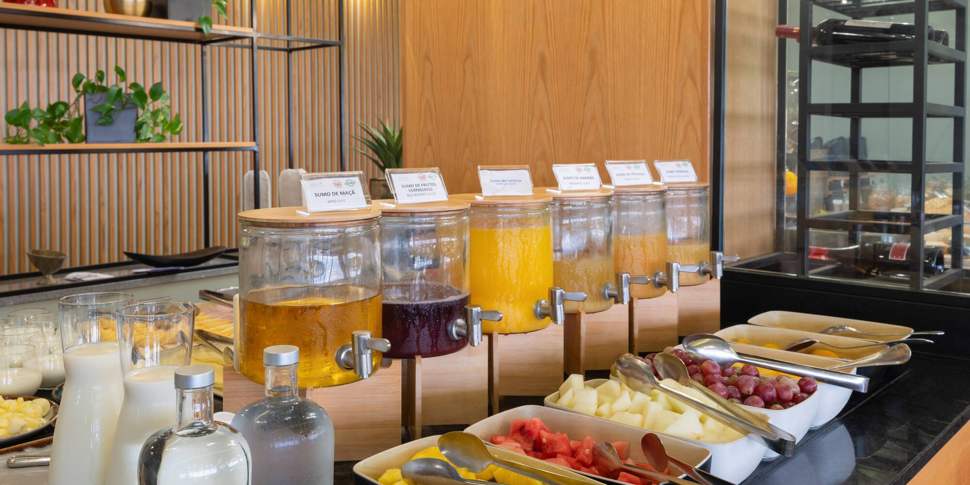 Breakfast buffet with fresh fruit juice dispensers, cut fruit, and milk.