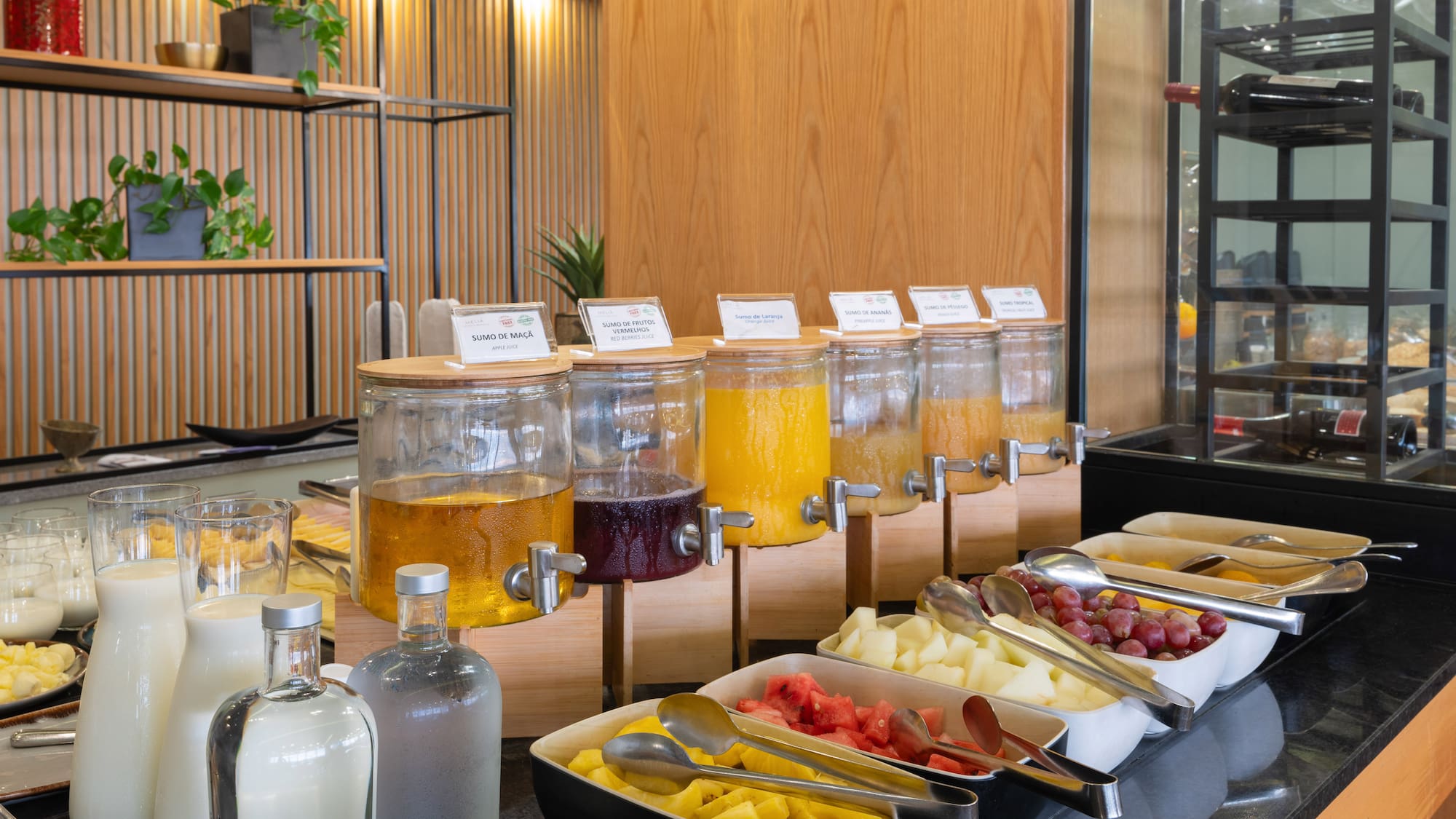 Breakfast buffet with fresh fruit juice dispensers, cut fruit, and milk.