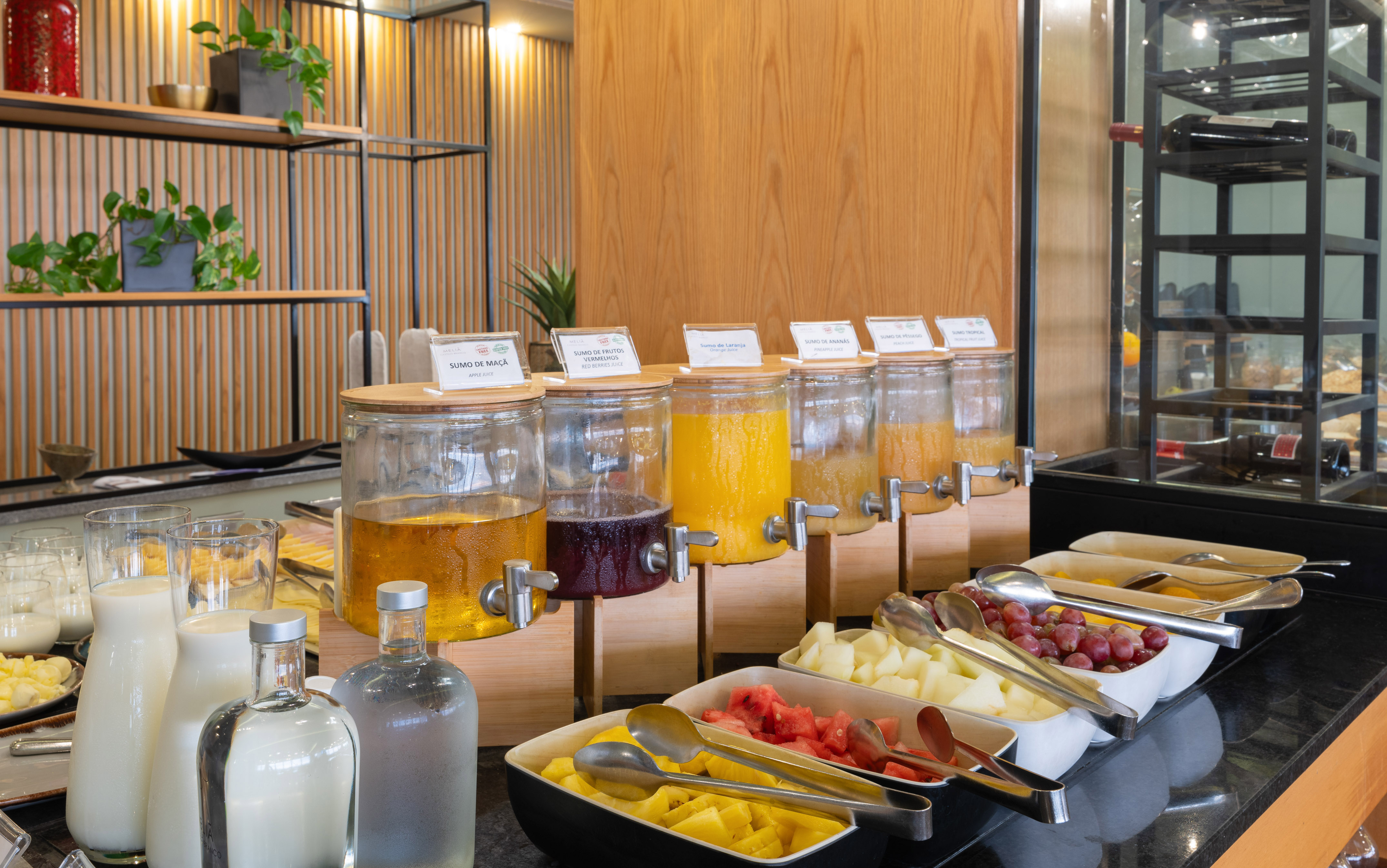 Breakfast buffet with fresh fruit juice dispensers, cut fruit, and milk.