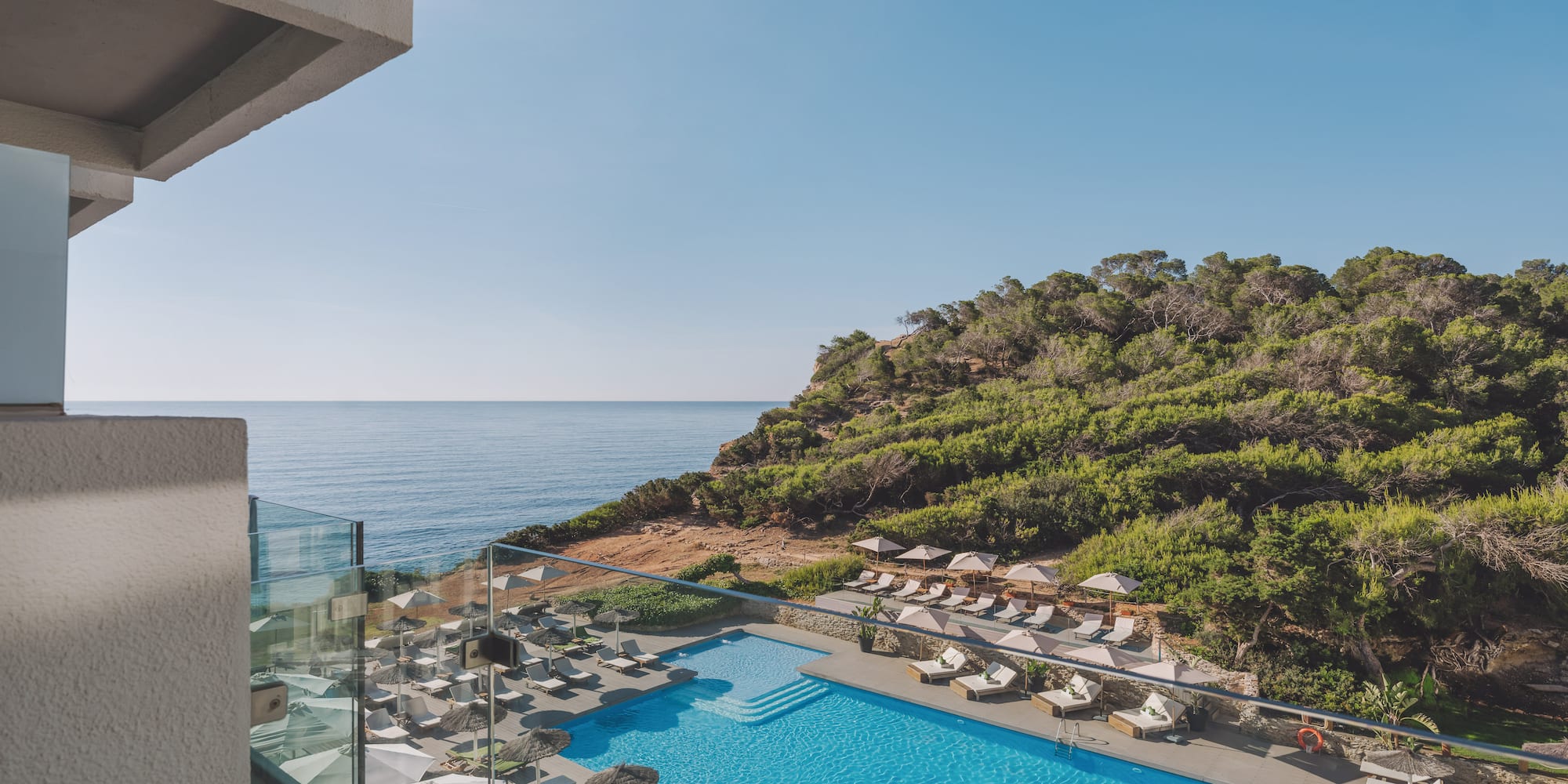 Hotel resort pool with ocean view, lush green cliffside from balcony.