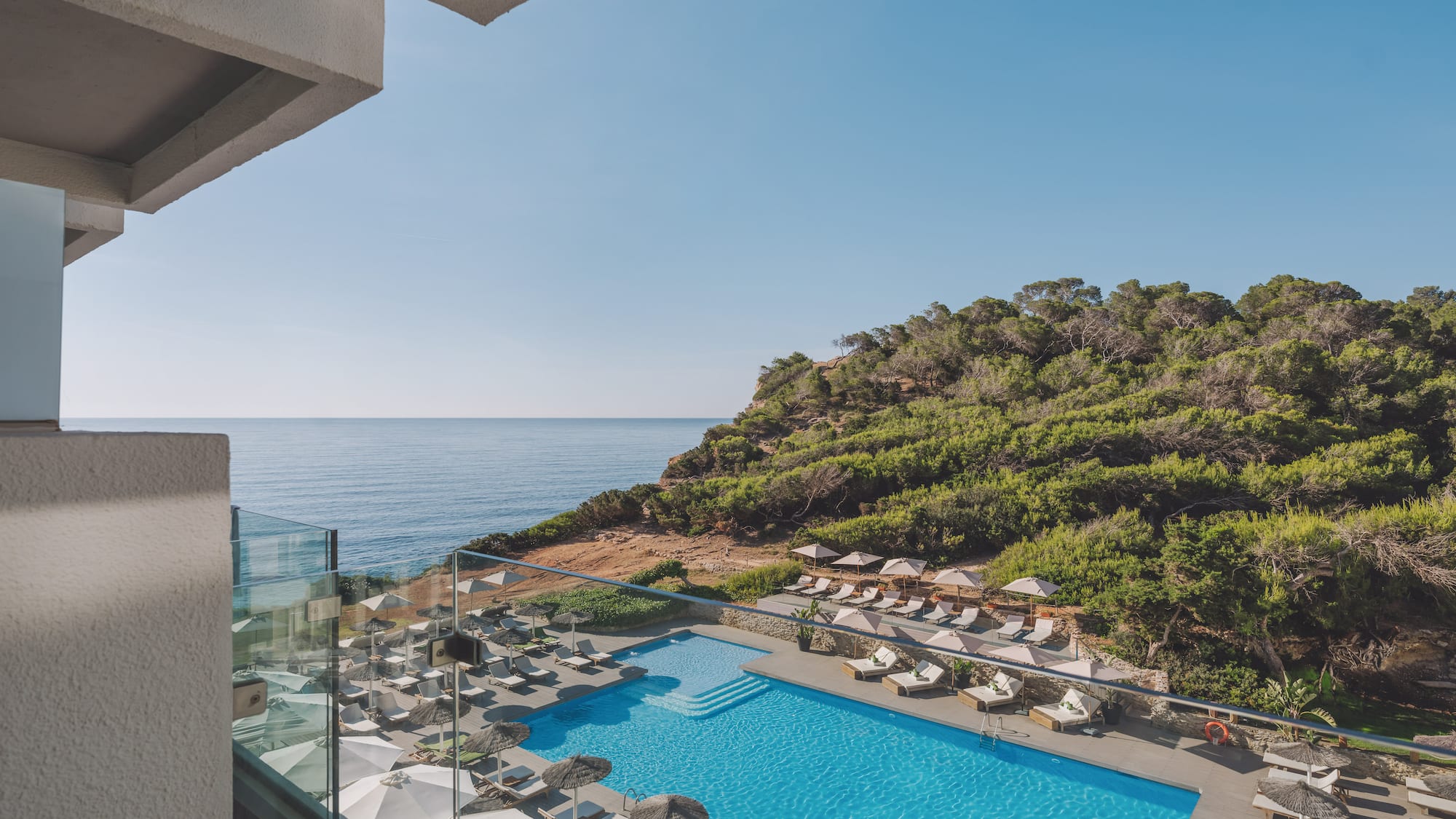 Hotel resort pool with ocean view, lush green cliffside from balcony.