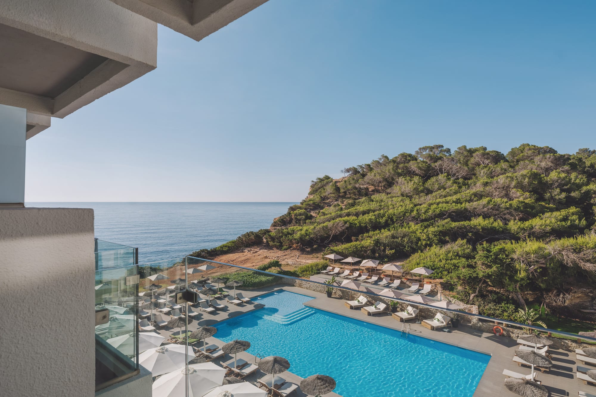 Hotel resort pool with ocean view, lush green cliffside from balcony.