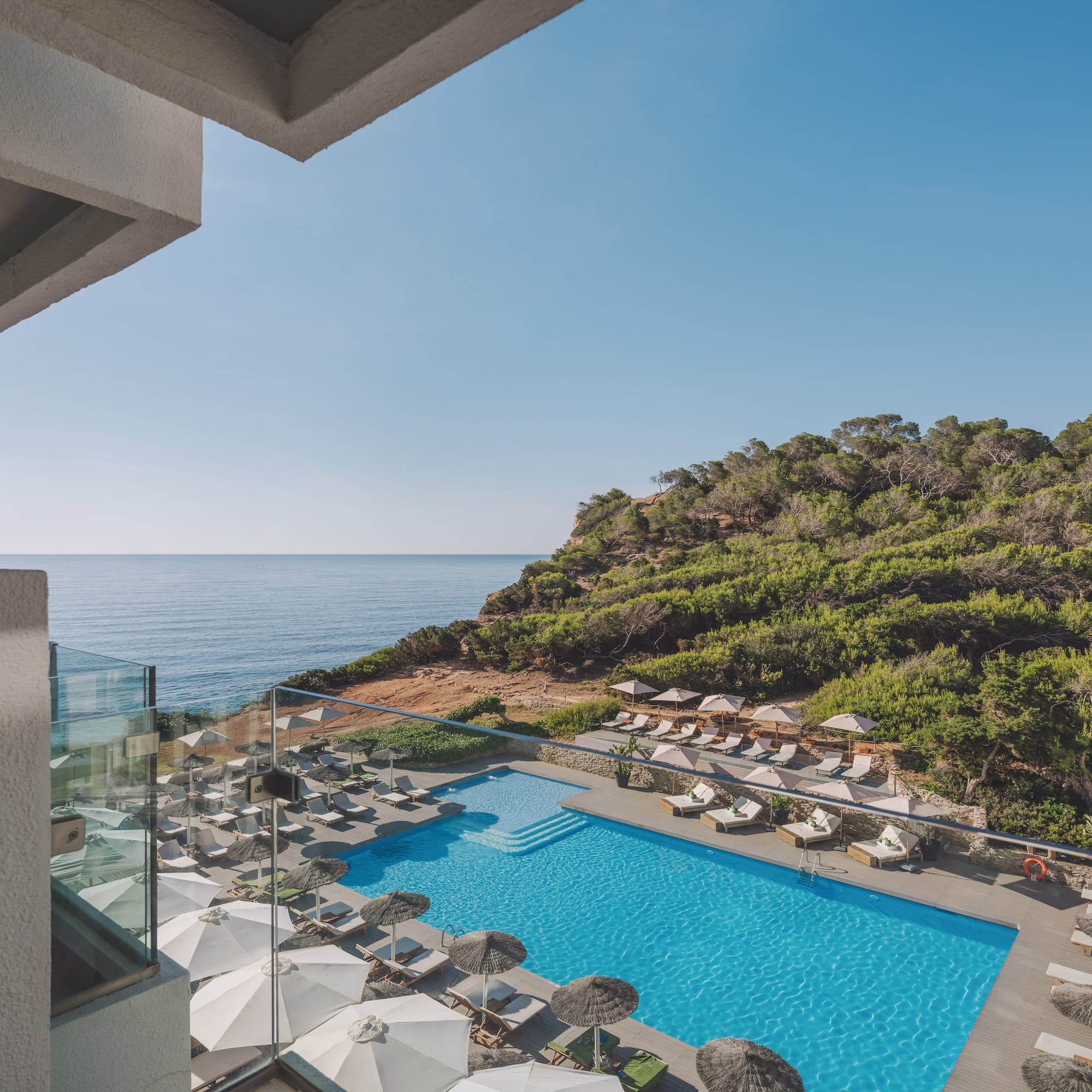 Hotel resort pool with ocean view, lush green cliffside from balcony.