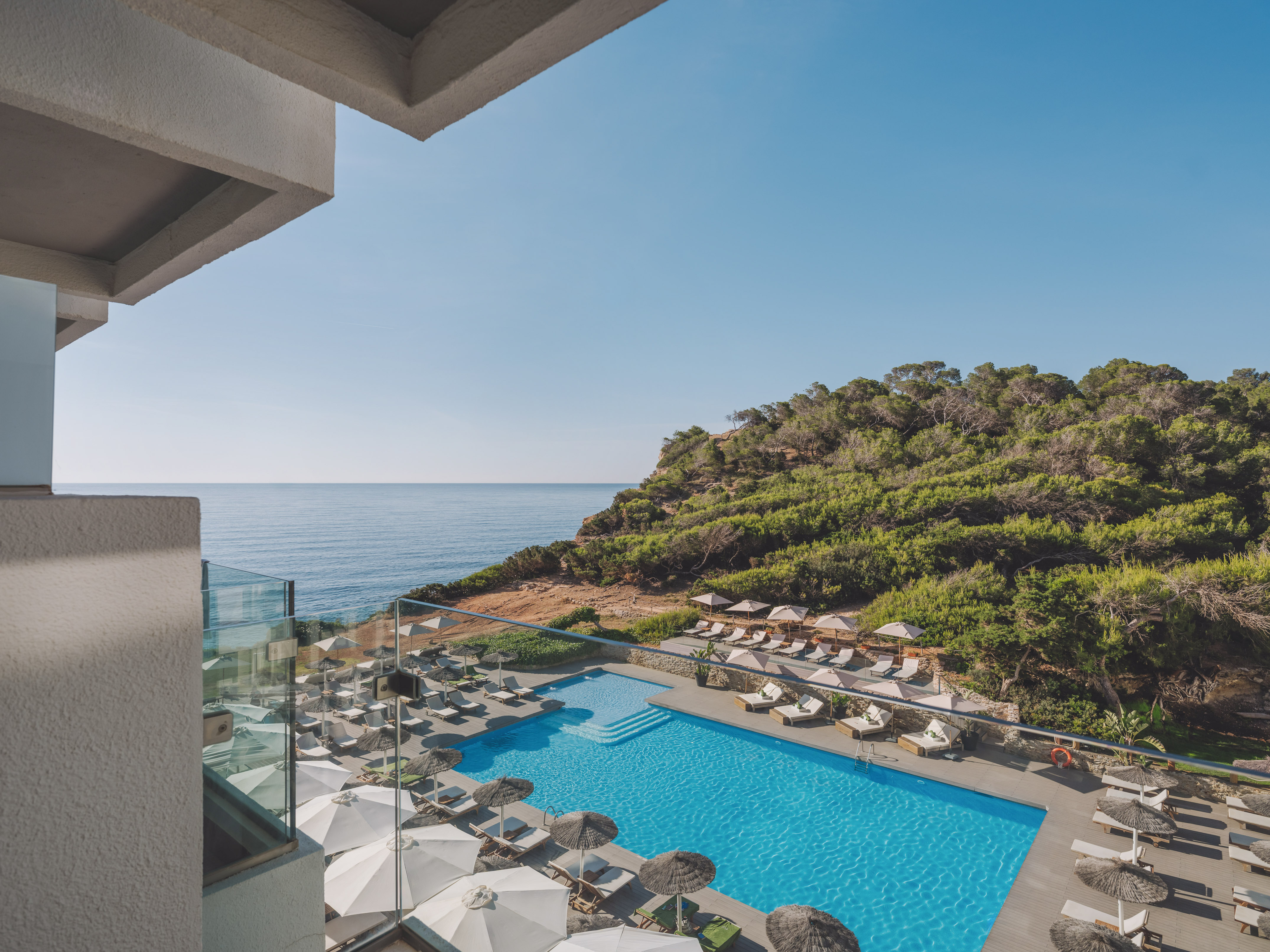 Hotel resort pool with ocean view, lush green cliffside from balcony.