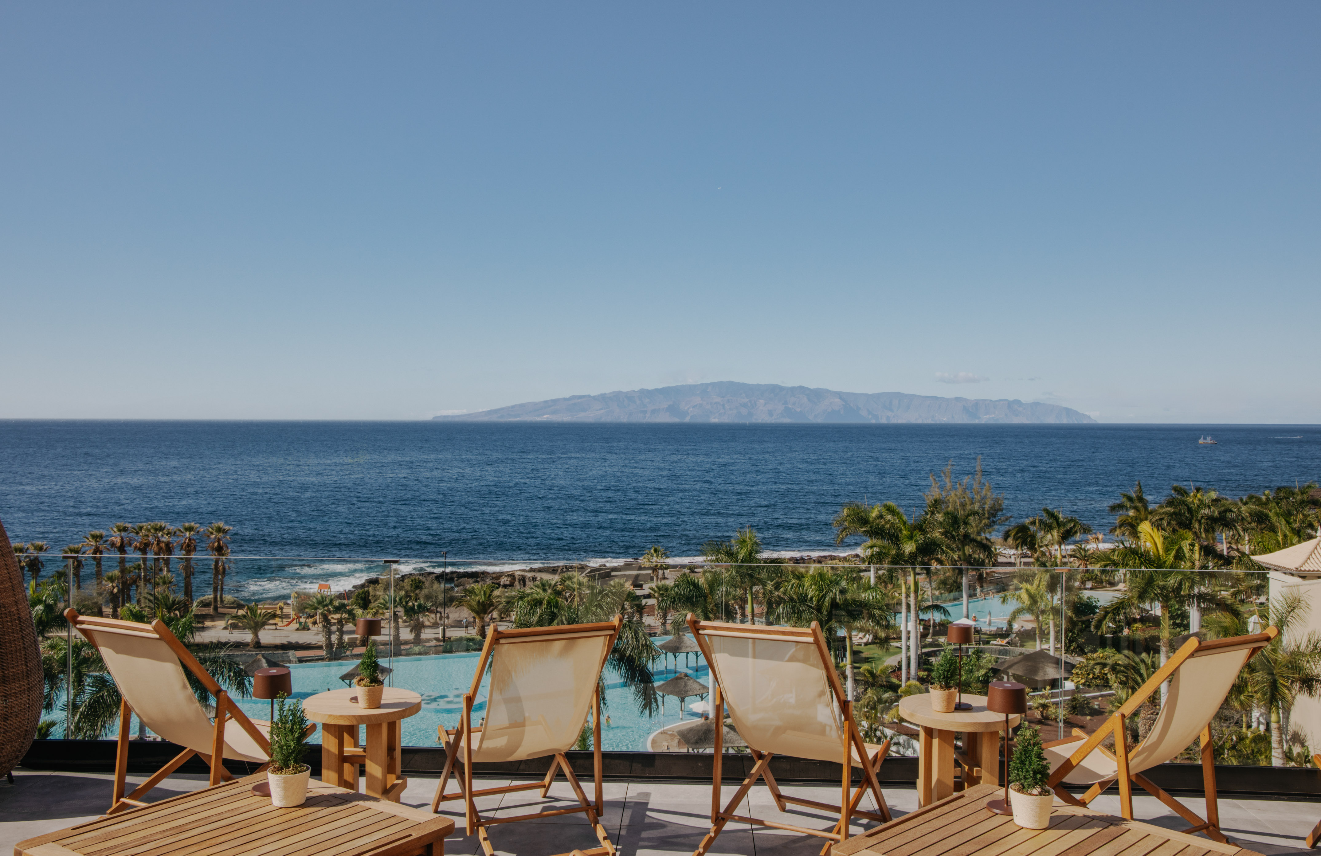 Resort balcony with ocean, distant island, lounge chairs, and pool view.