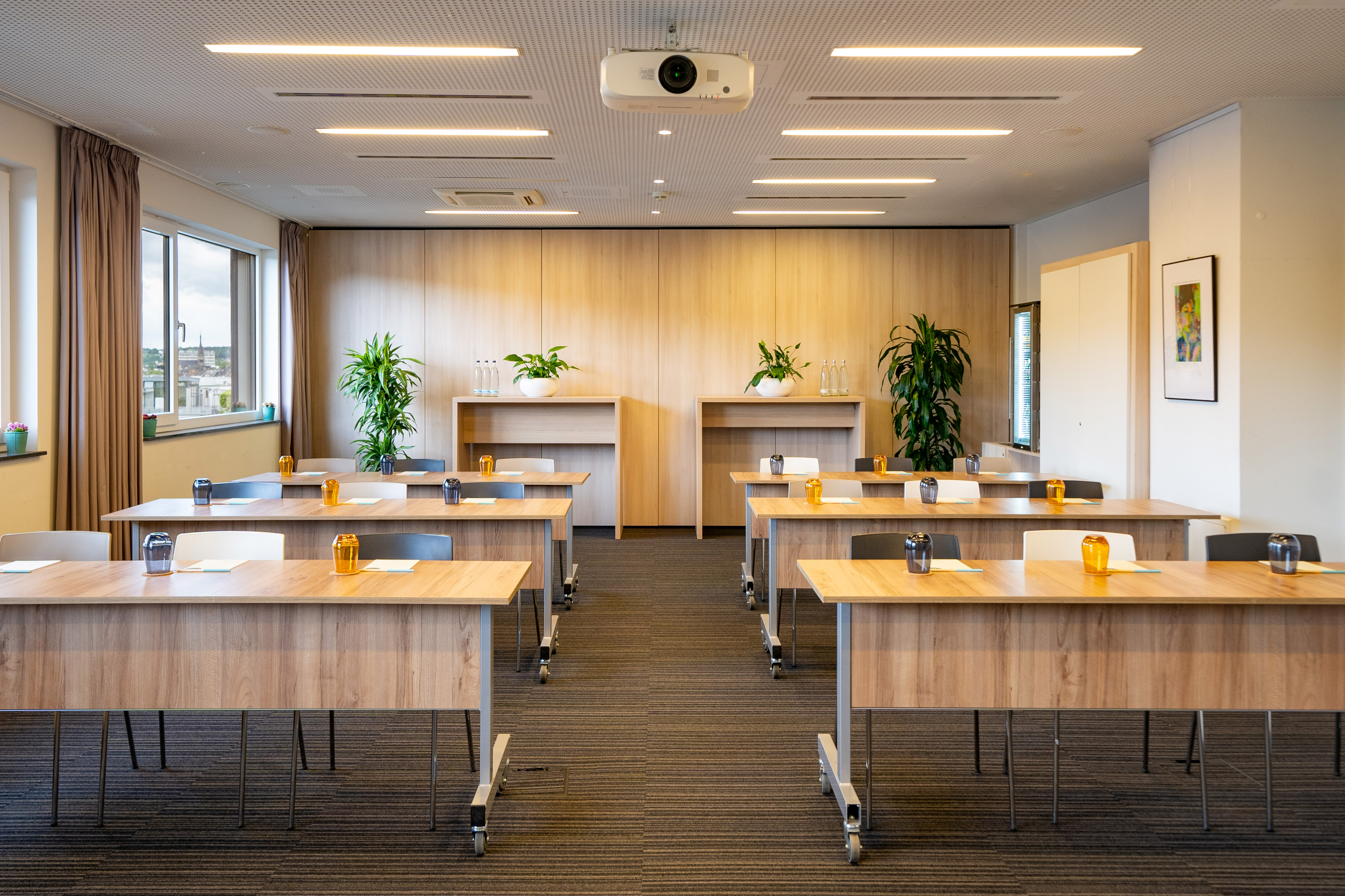 Modern training room with flexible tables, chairs, a projector, and plants.