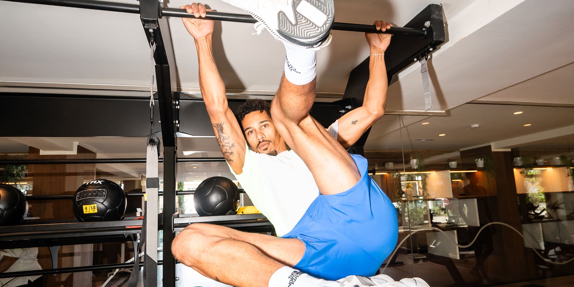 Athletic man inverted on gym pull-up bar, performing core exercise.