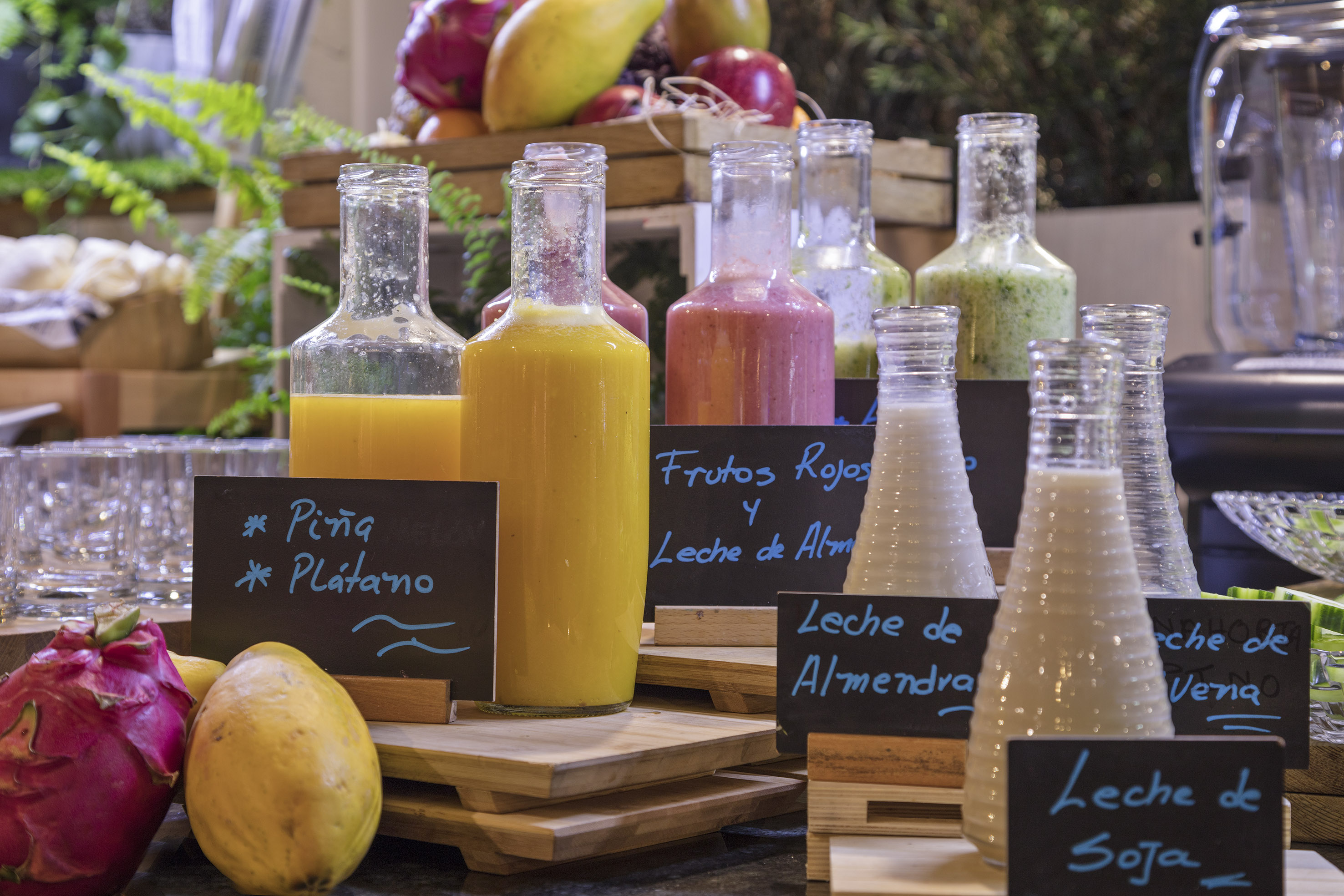 Variety of fresh fruit juices and plant-based milks in bottles at a buffet.