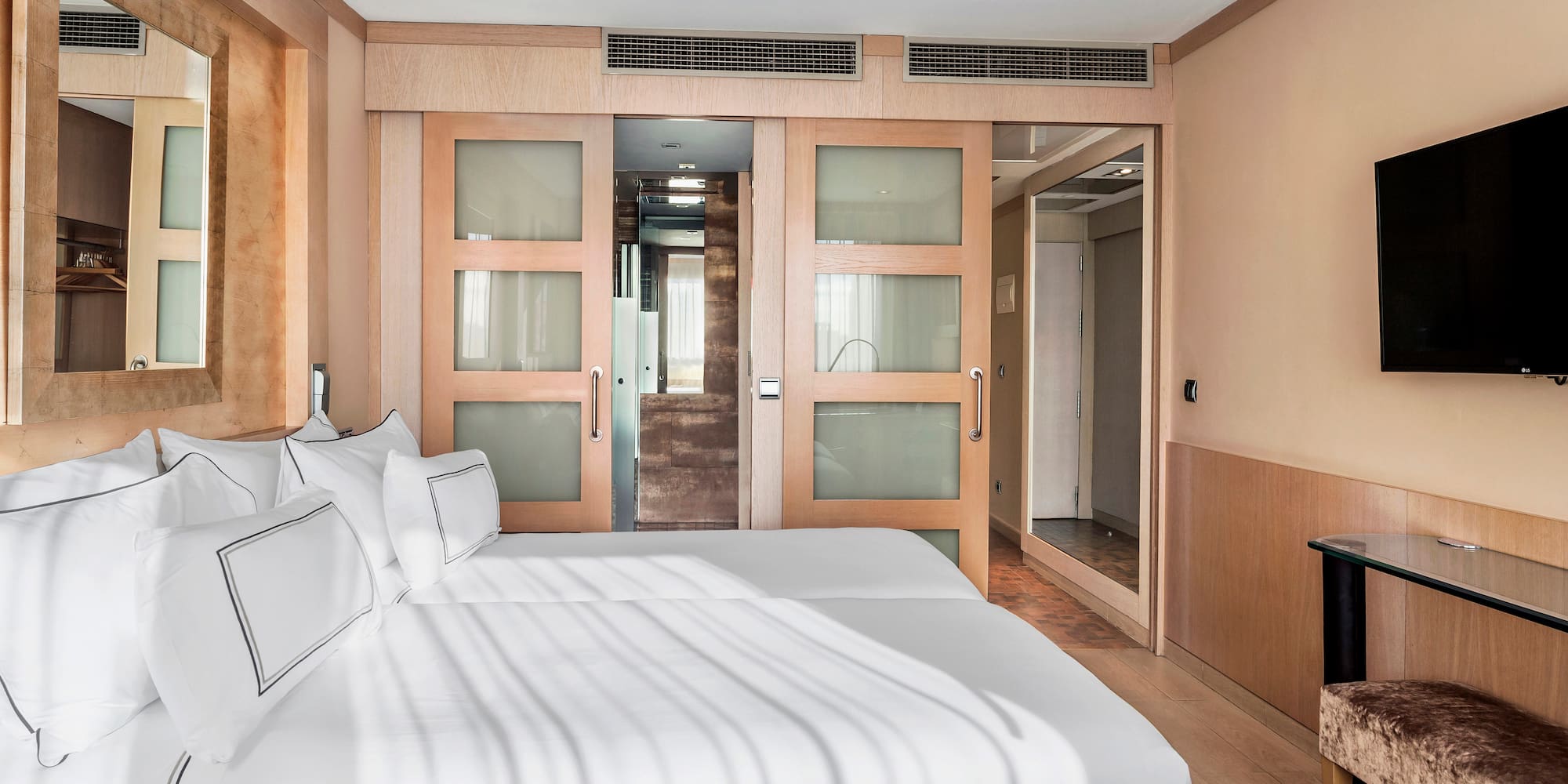 Modern hotel room with two beds, wooden sliding doors, and flat-screen TV.