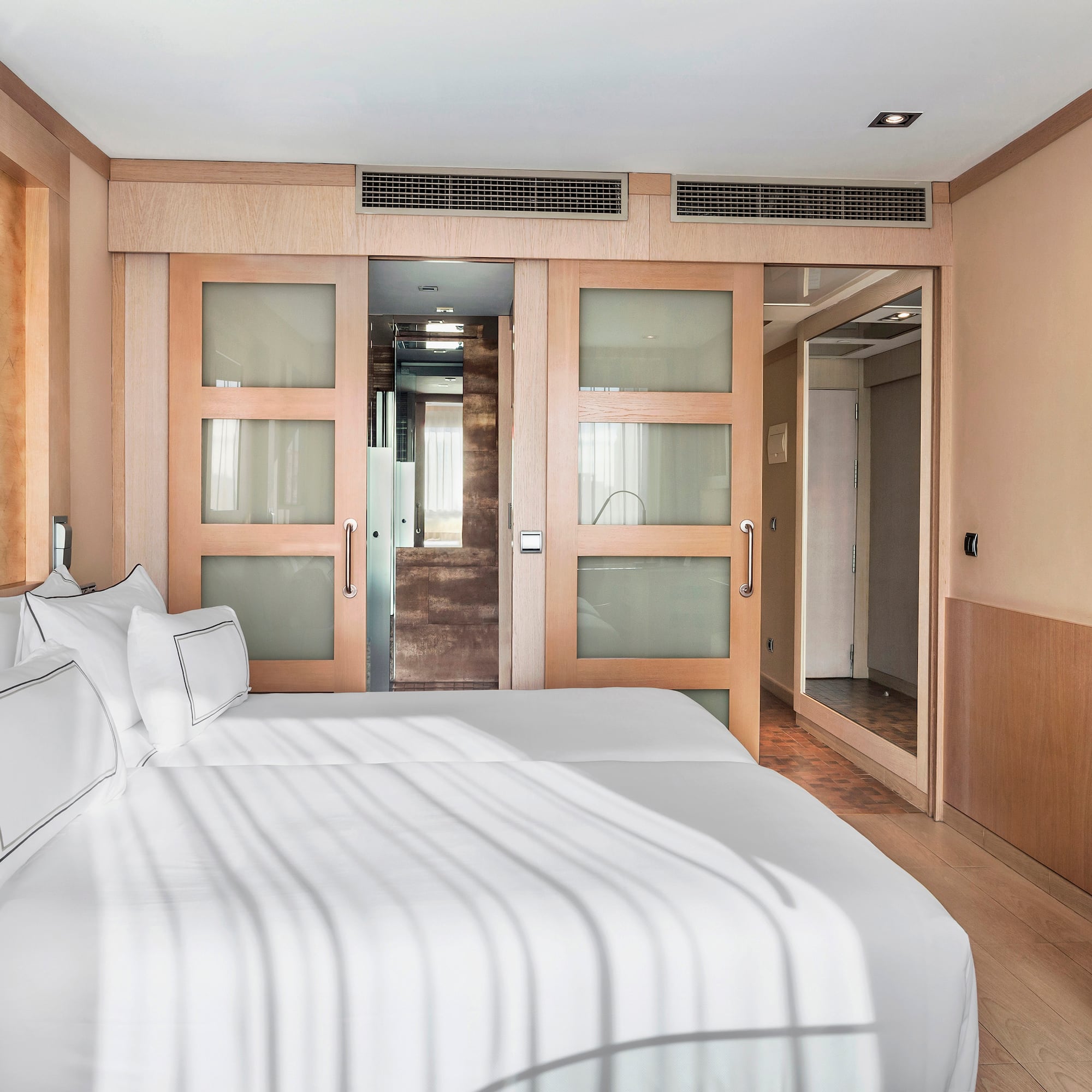 Modern hotel room with two beds, wooden sliding doors, and flat-screen TV.
