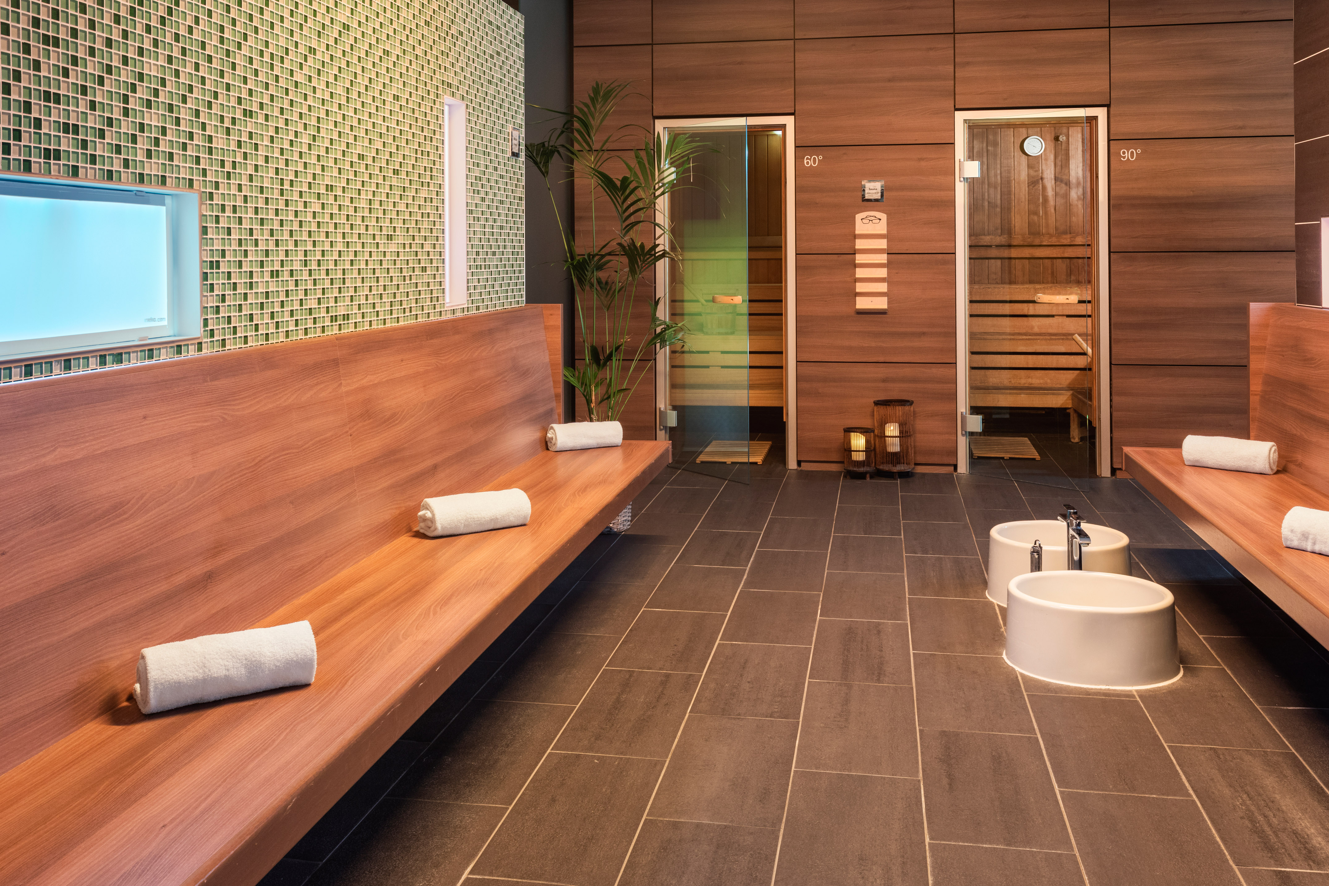 Modern spa sauna area with wooden benches, foot baths, and two saunas.