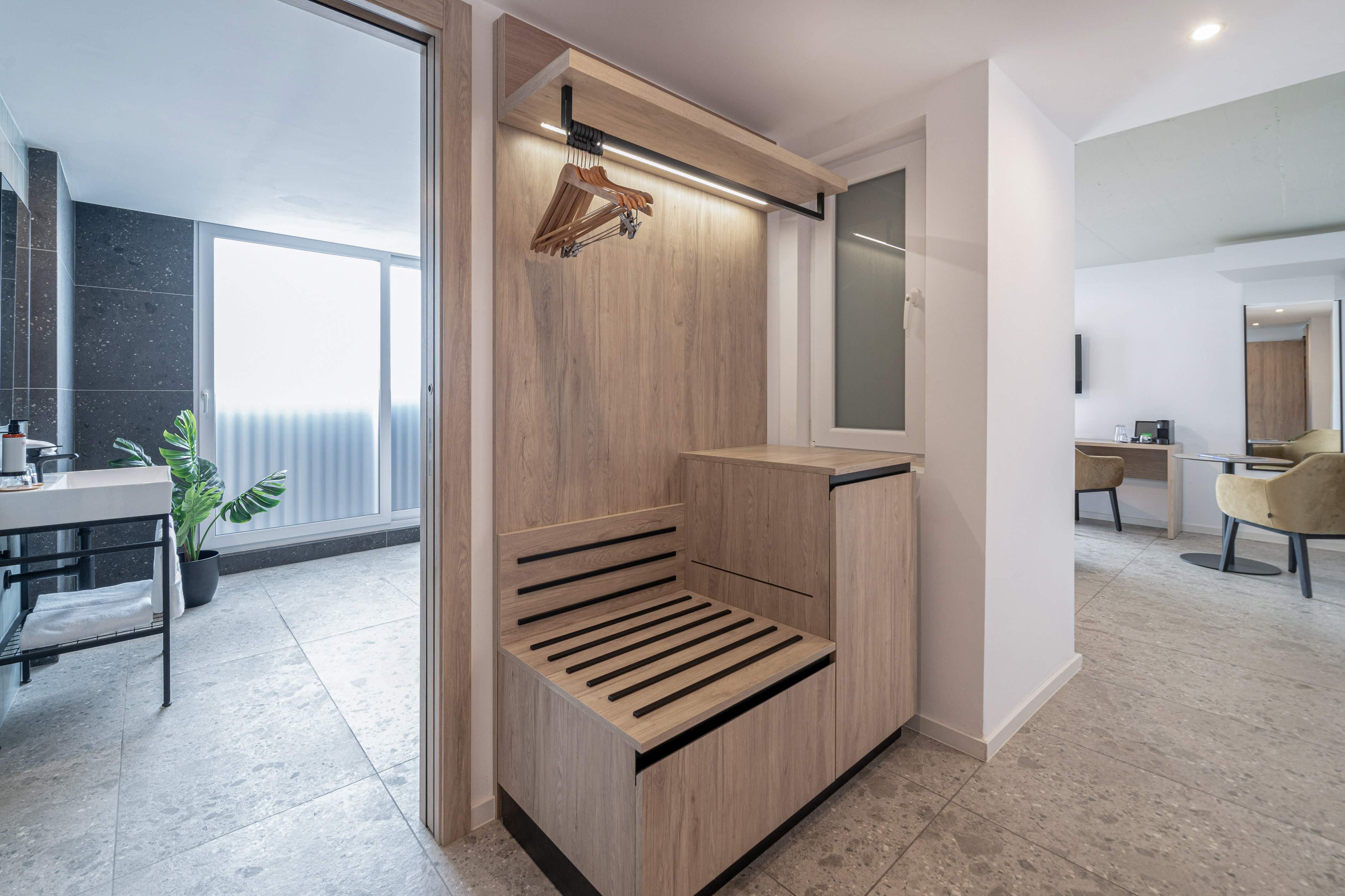 Modern hotel room entryway with wooden wardrobe, luggage rack, and bathroom access.