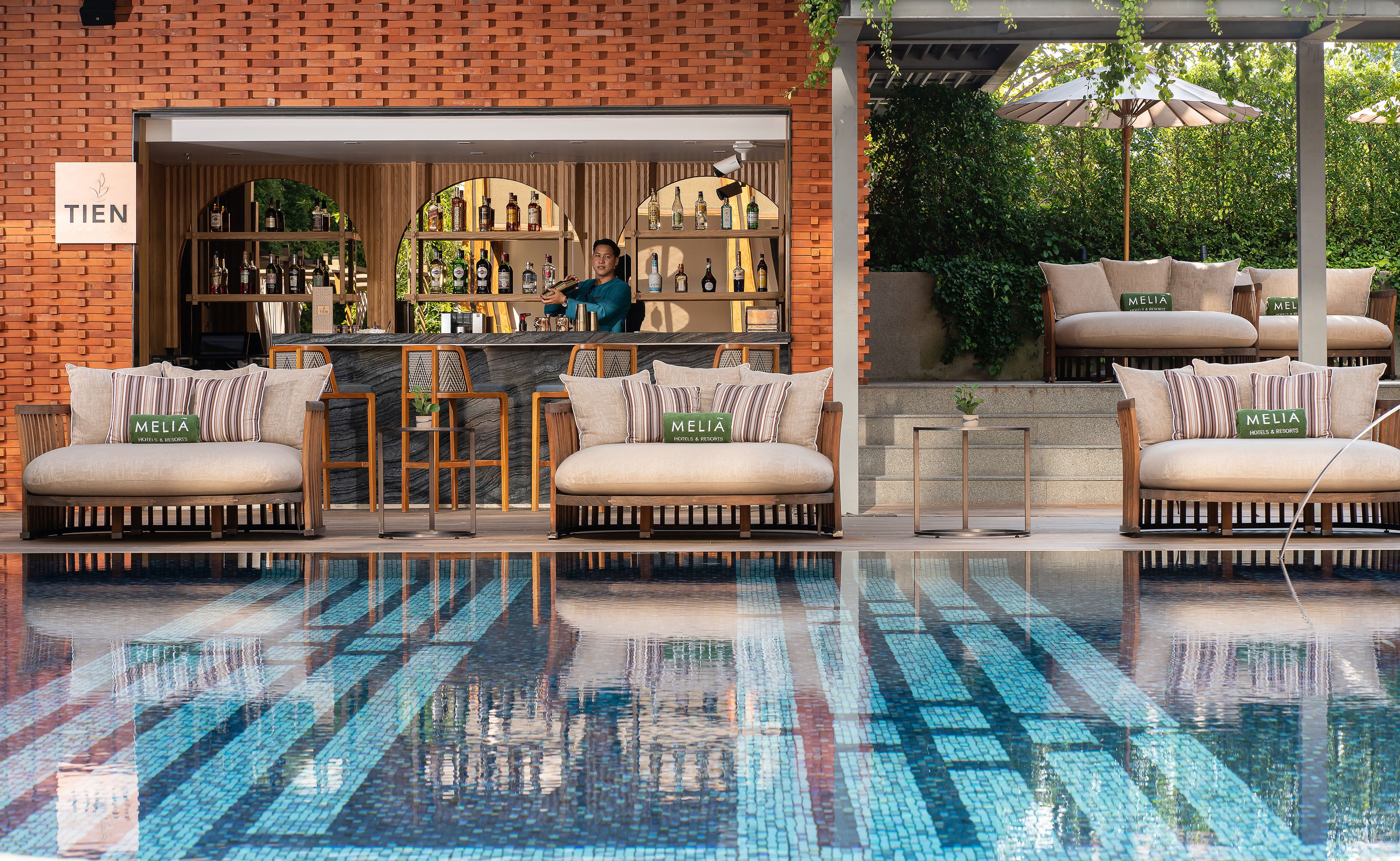 Meliá Hotels & Resorts poolside bar with bartender, lounge seating, and swimming pool.