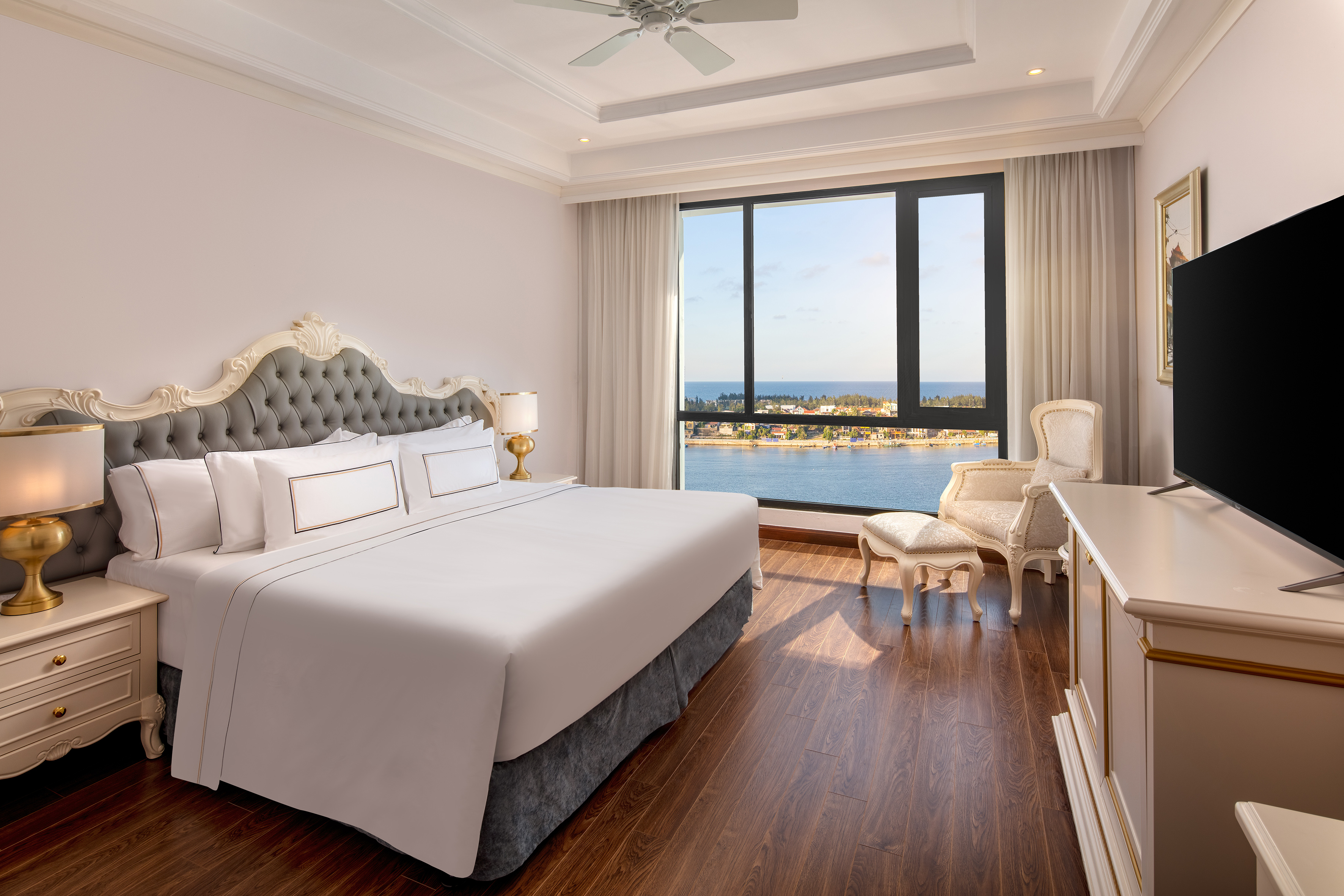 Elegant hotel bedroom with king bed, ocean view, and ornate tufted headboard.