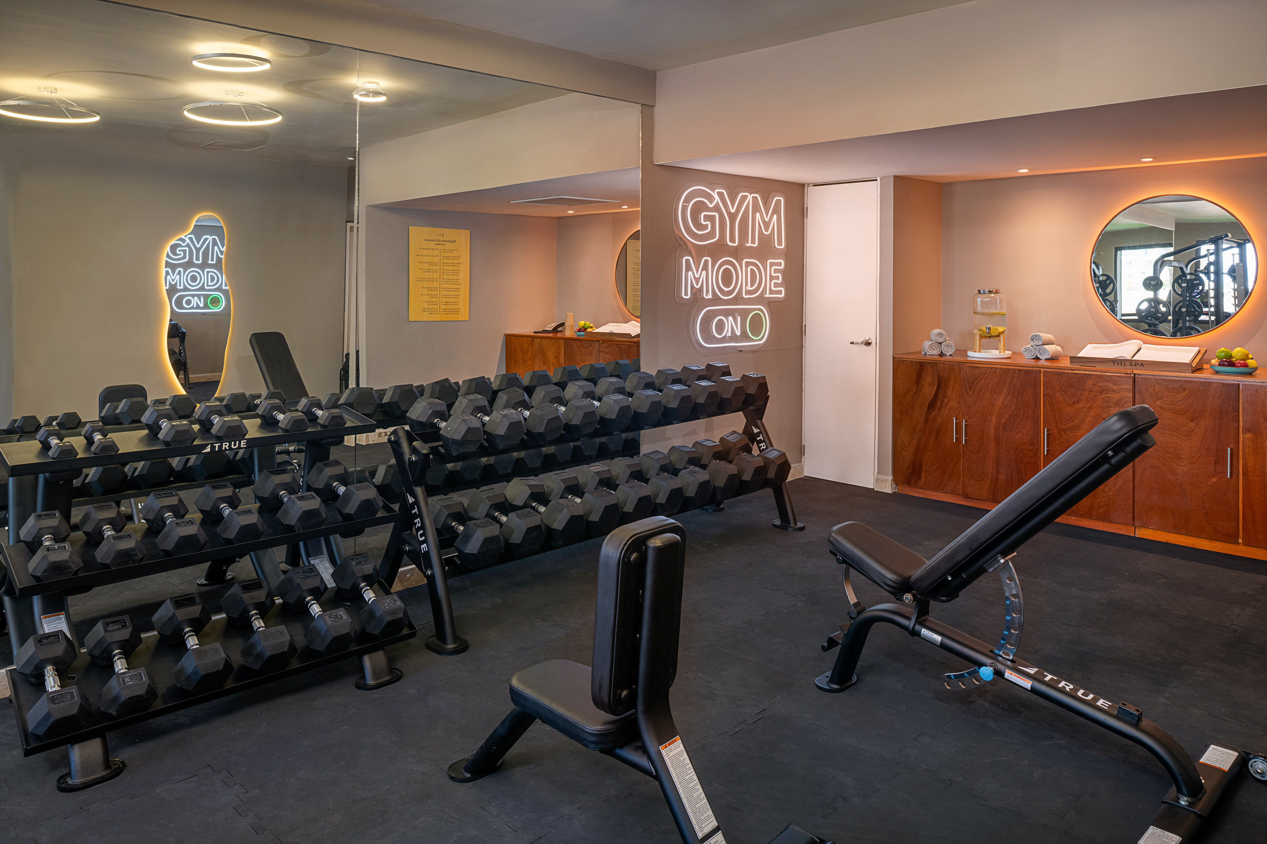 Fitness room with full dumbbell sets, benches, and "GYM MODE ON" neon light.