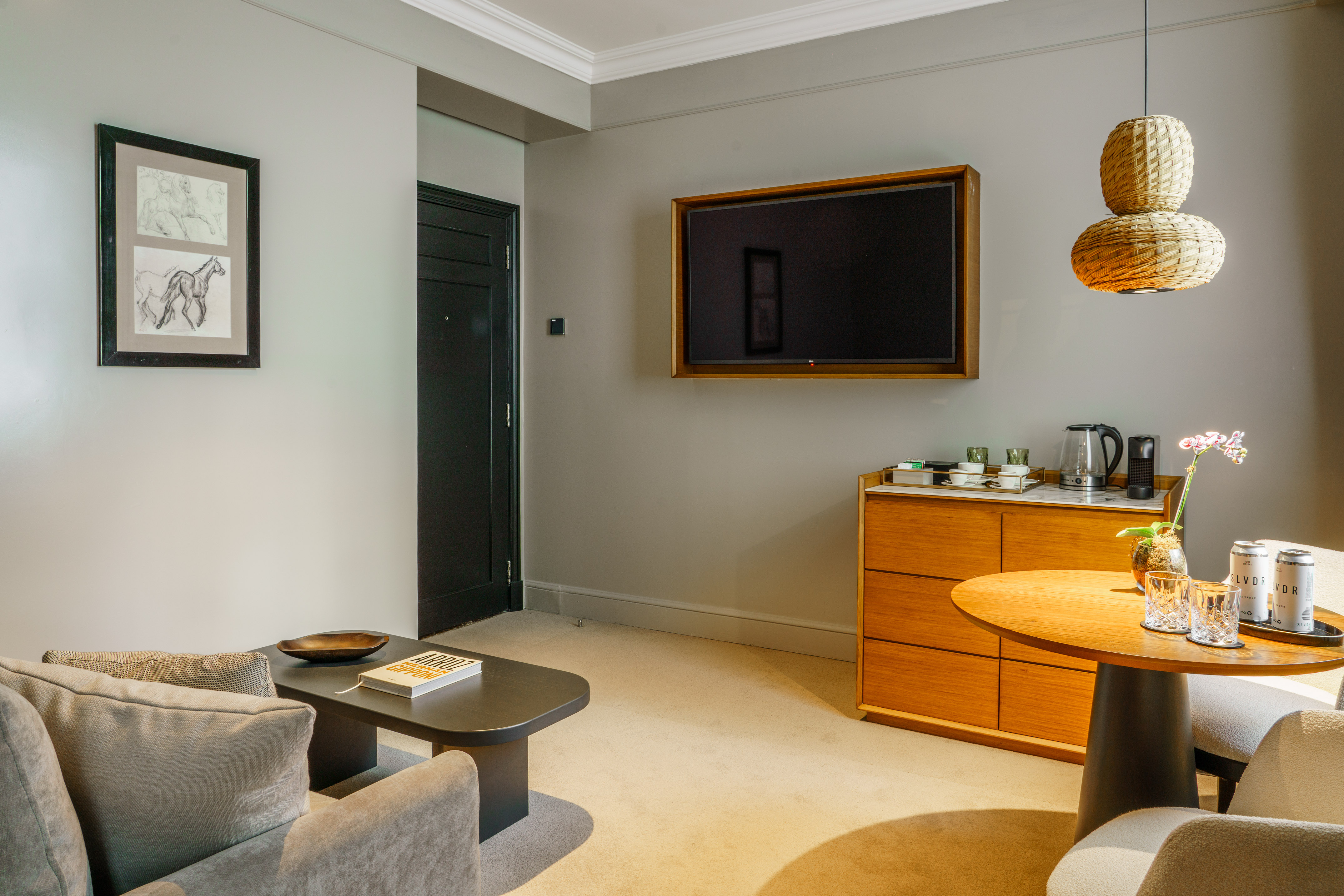 Modern hotel suite living area with gray sofa, flat-screen TV, and wooden furnishings.