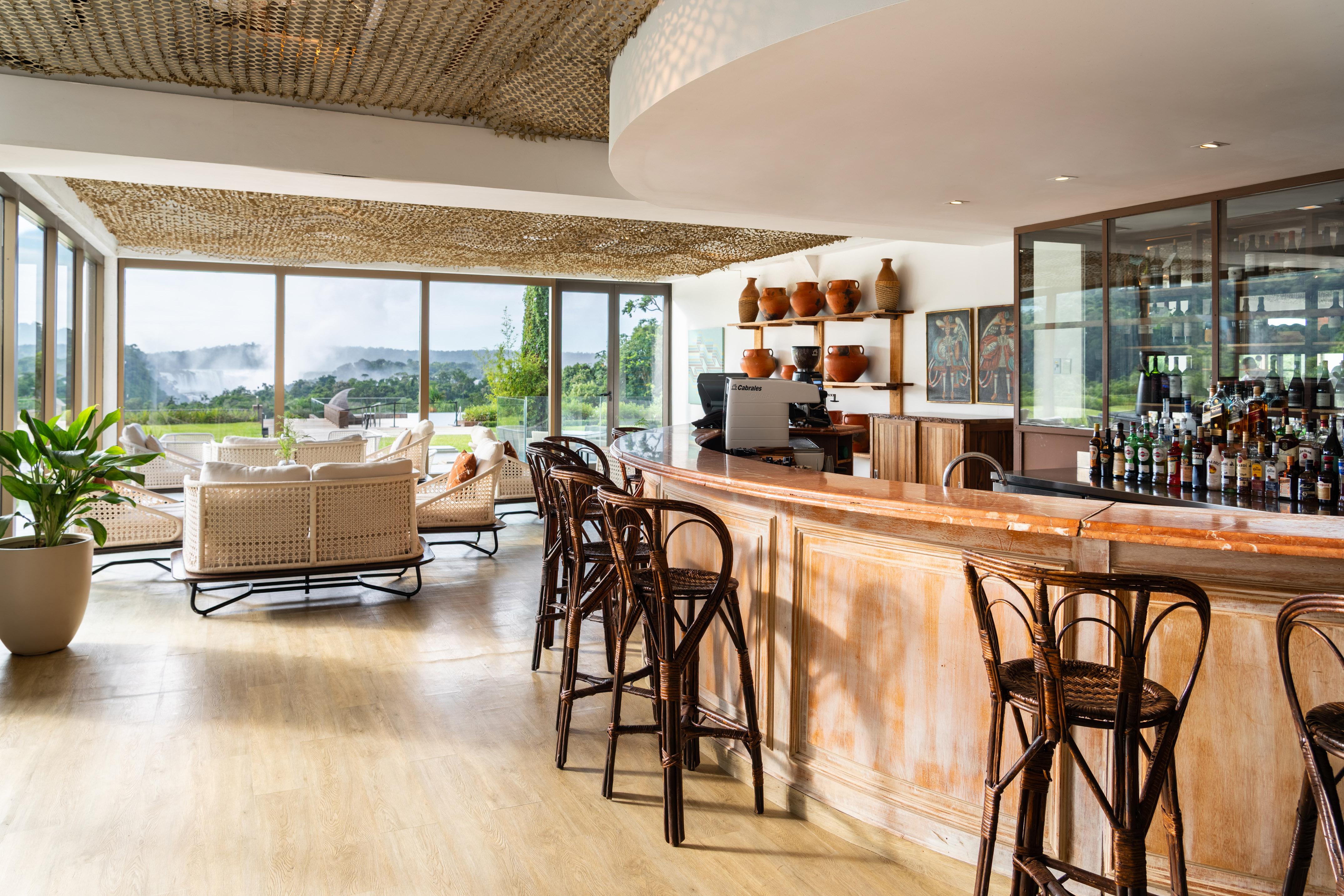 Luxury resort bar with wicker seating, panoramic waterfall view, and liquor display.