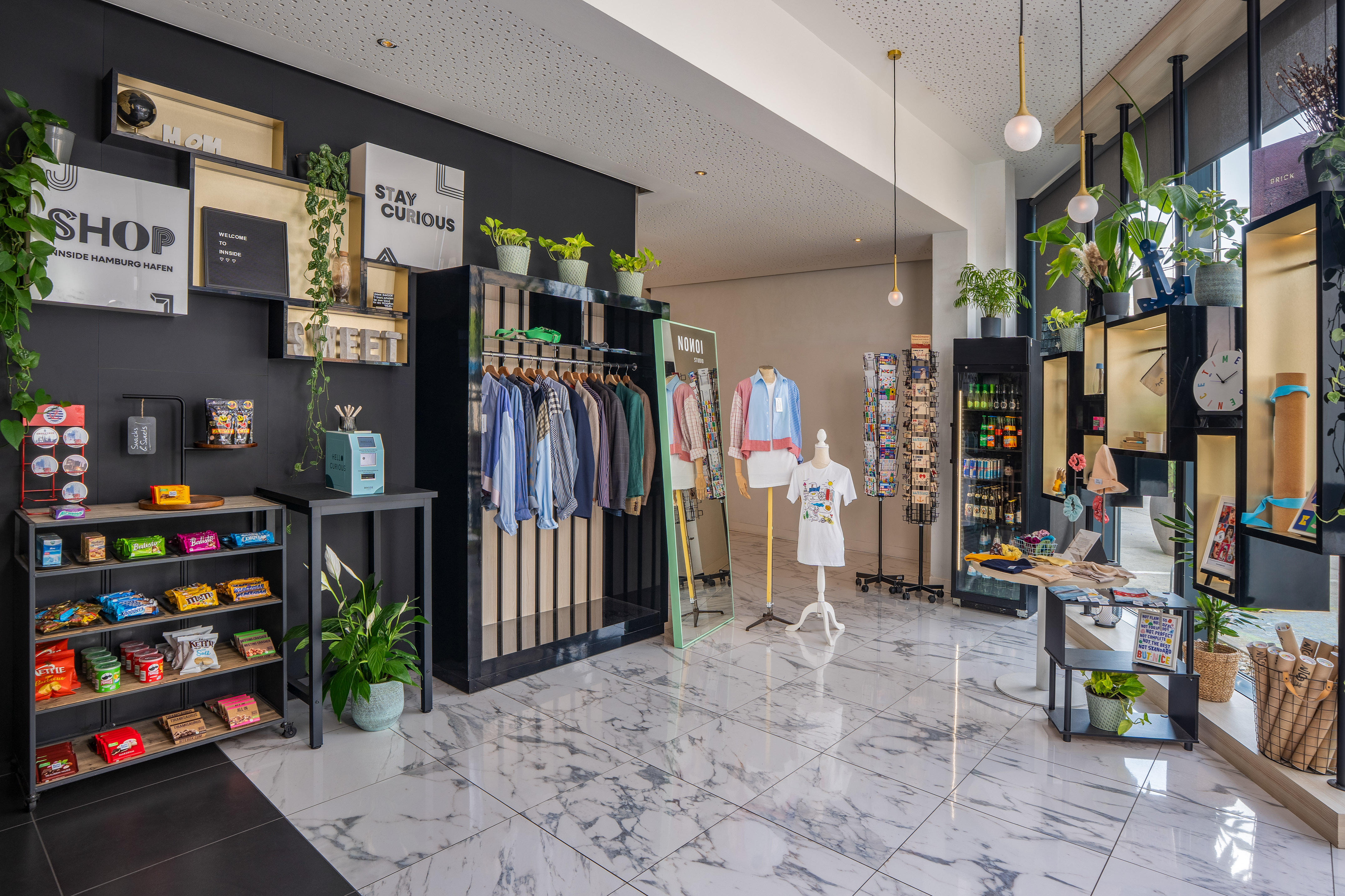 Modern hotel lobby shop with snacks, clothing, diverse decor, and "Stay Curious" sign.