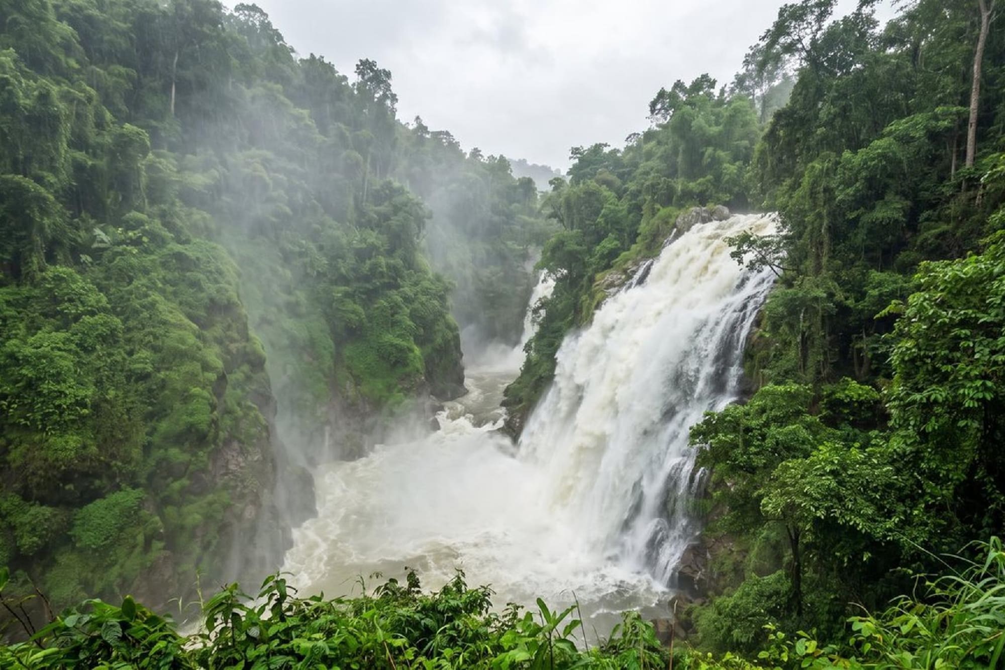 Powerful waterfall in a lush green tropical forest with rising mist.