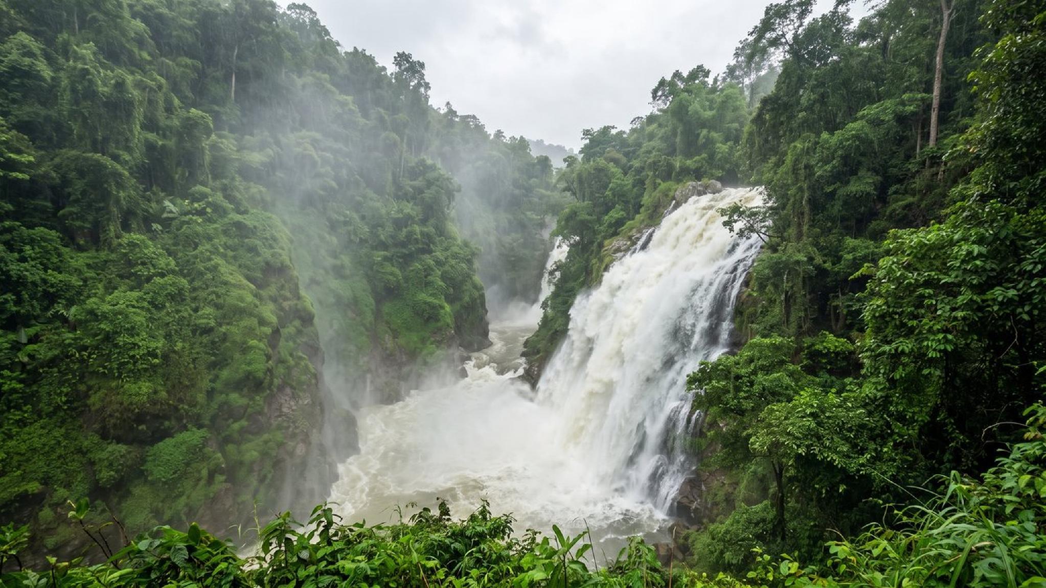 Powerful waterfall in a lush green tropical forest with rising mist.
