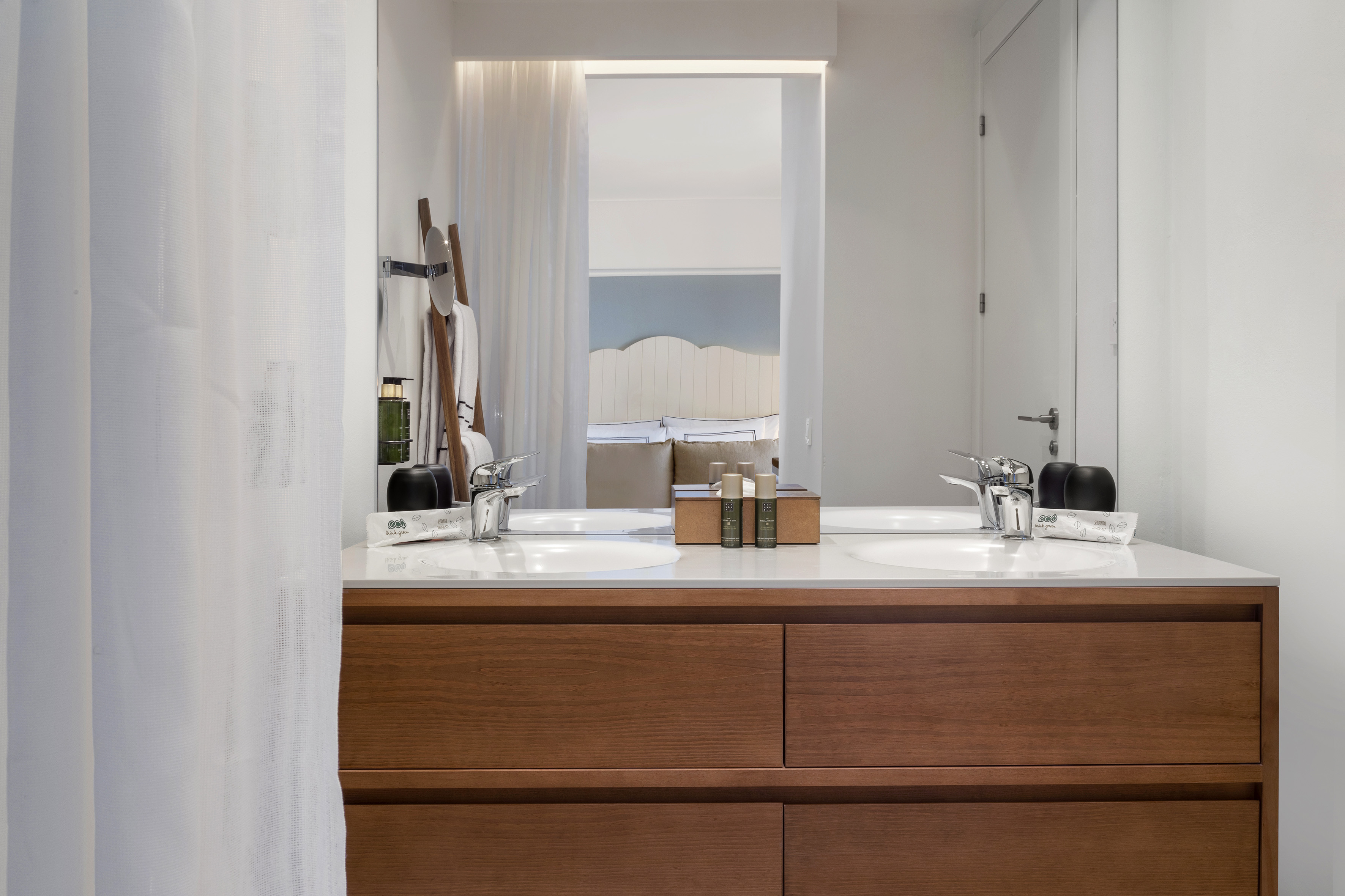 Sleek double-sink wood bathroom vanity reflecting a modern bedroom.