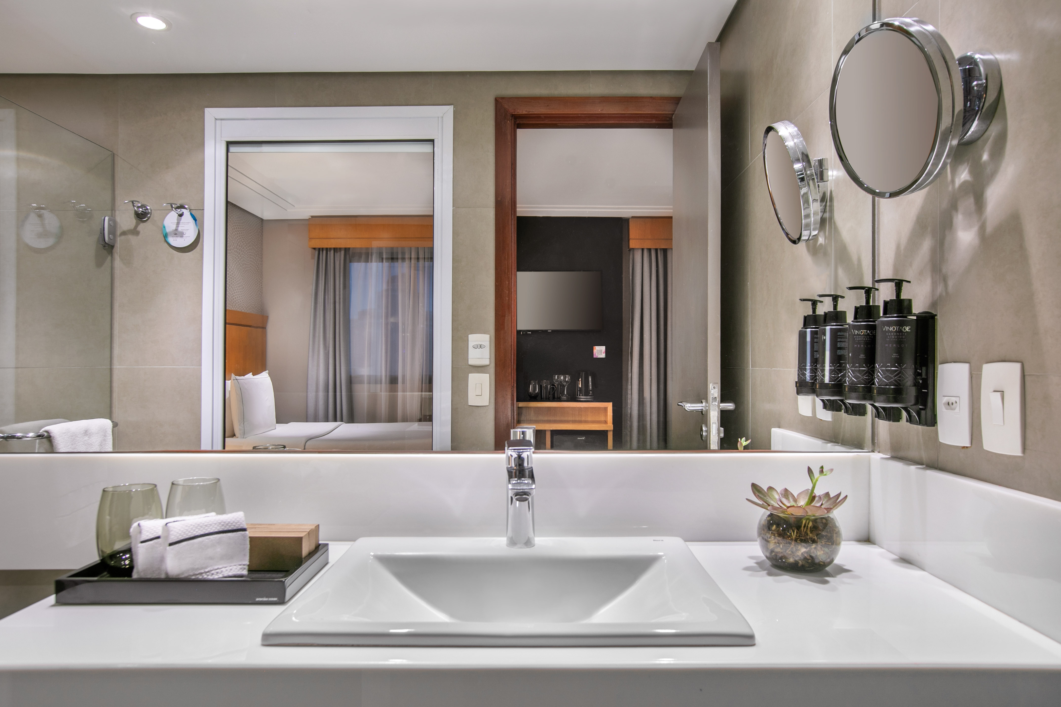 Sleek hotel bathroom vanity with white sink, mirror reflecting modern bedroom.
