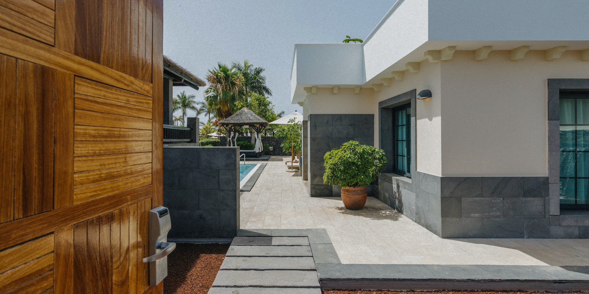 Wooden gate opens to modern luxury villa, private pool, and tropical garden.