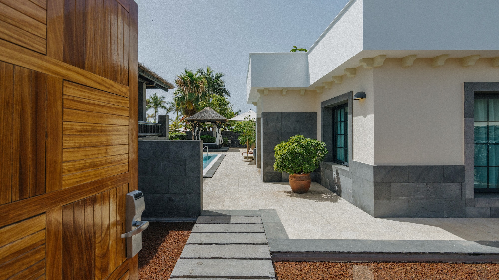 Wooden gate opens to modern luxury villa, private pool, and tropical garden.
