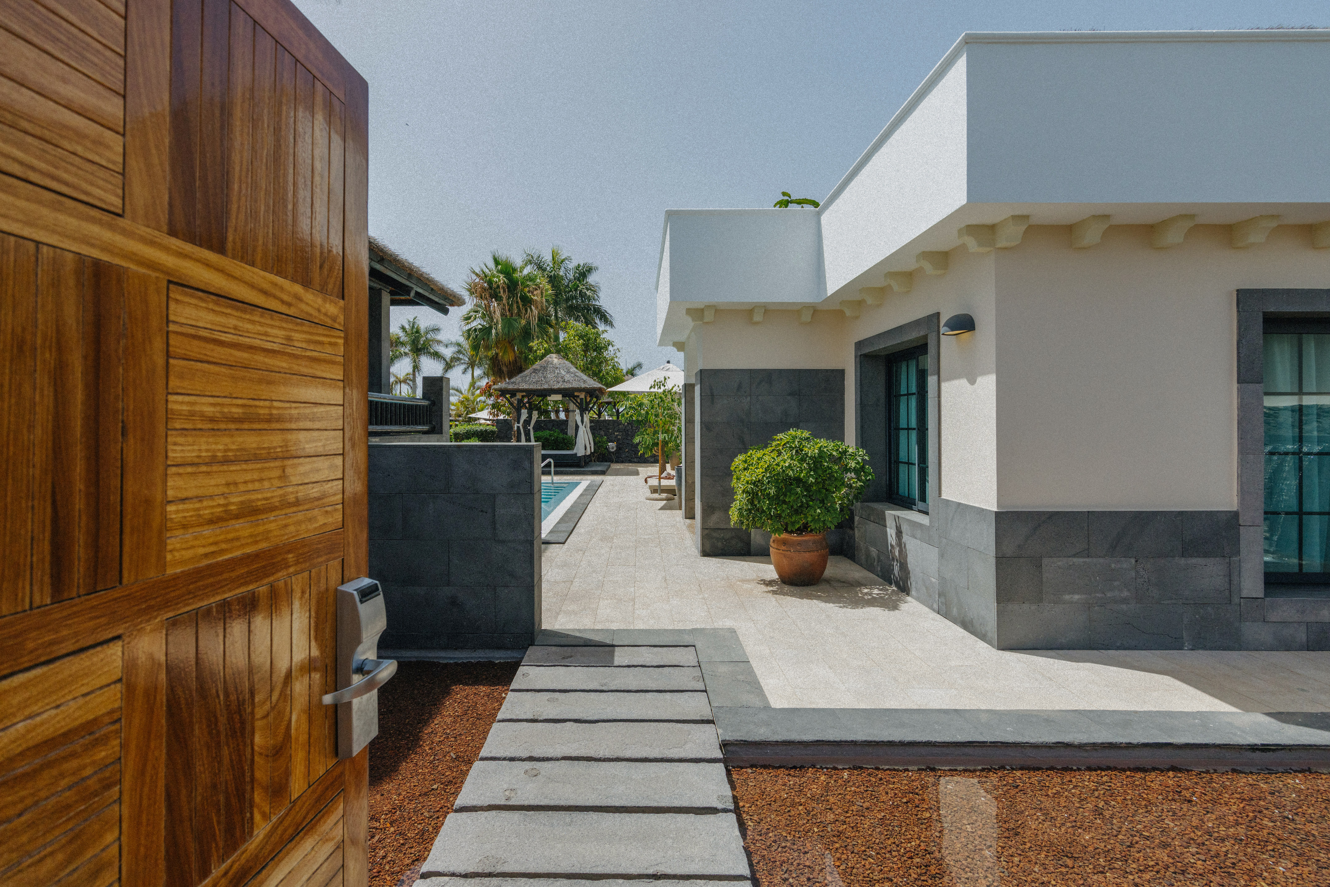 Wooden gate opens to modern luxury villa, private pool, and tropical garden.