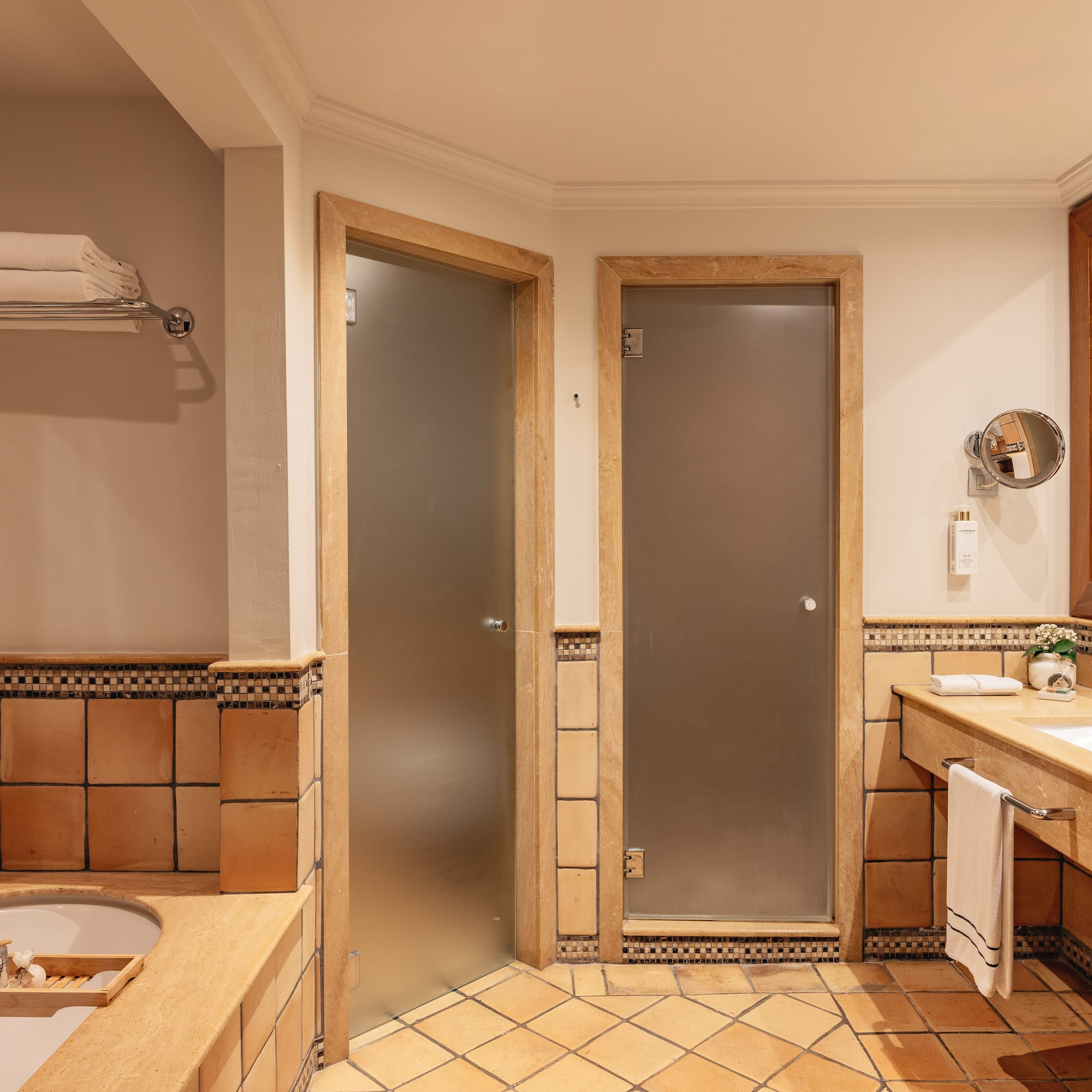 Hotel bathroom with terracotta tiles, double vanity, bathtub, and frosted glass doors.