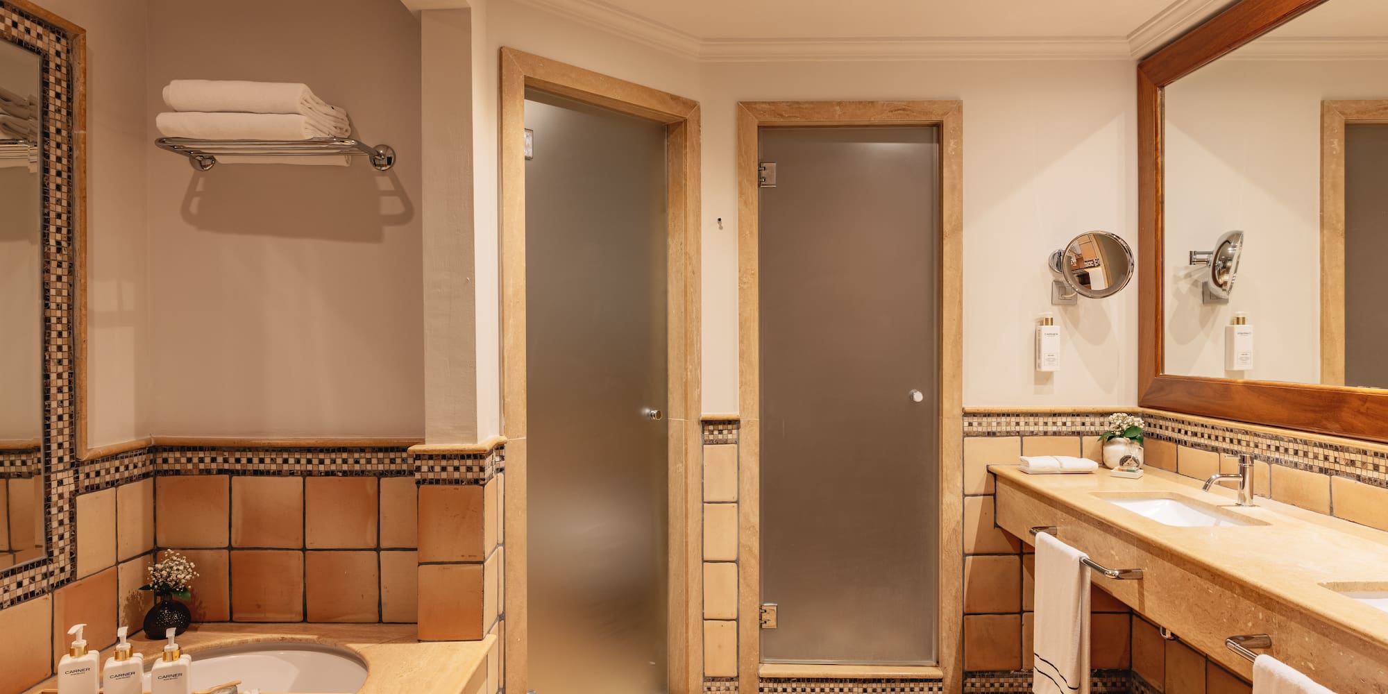 Hotel bathroom with terracotta tiles, double vanity, bathtub, and frosted glass doors.