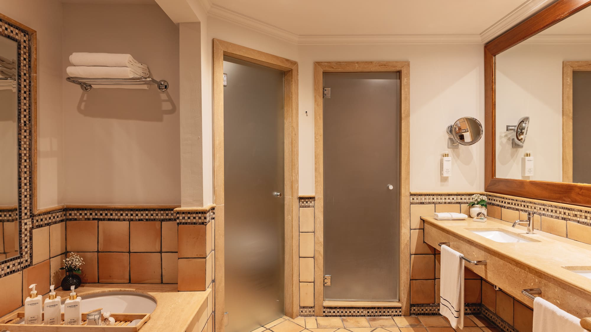 Hotel bathroom with terracotta tiles, double vanity, bathtub, and frosted glass doors.