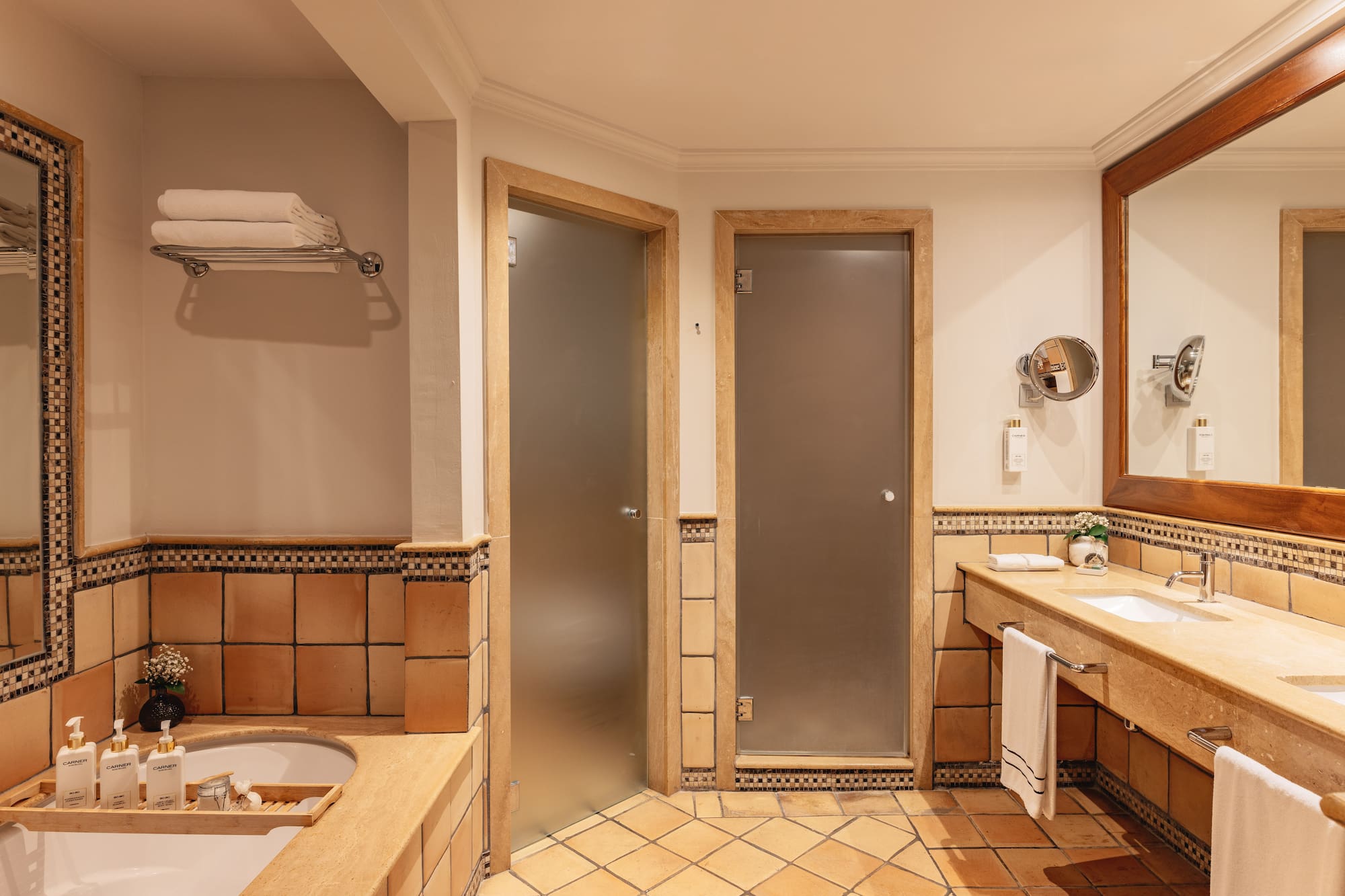 Hotel bathroom with terracotta tiles, double vanity, bathtub, and frosted glass doors.