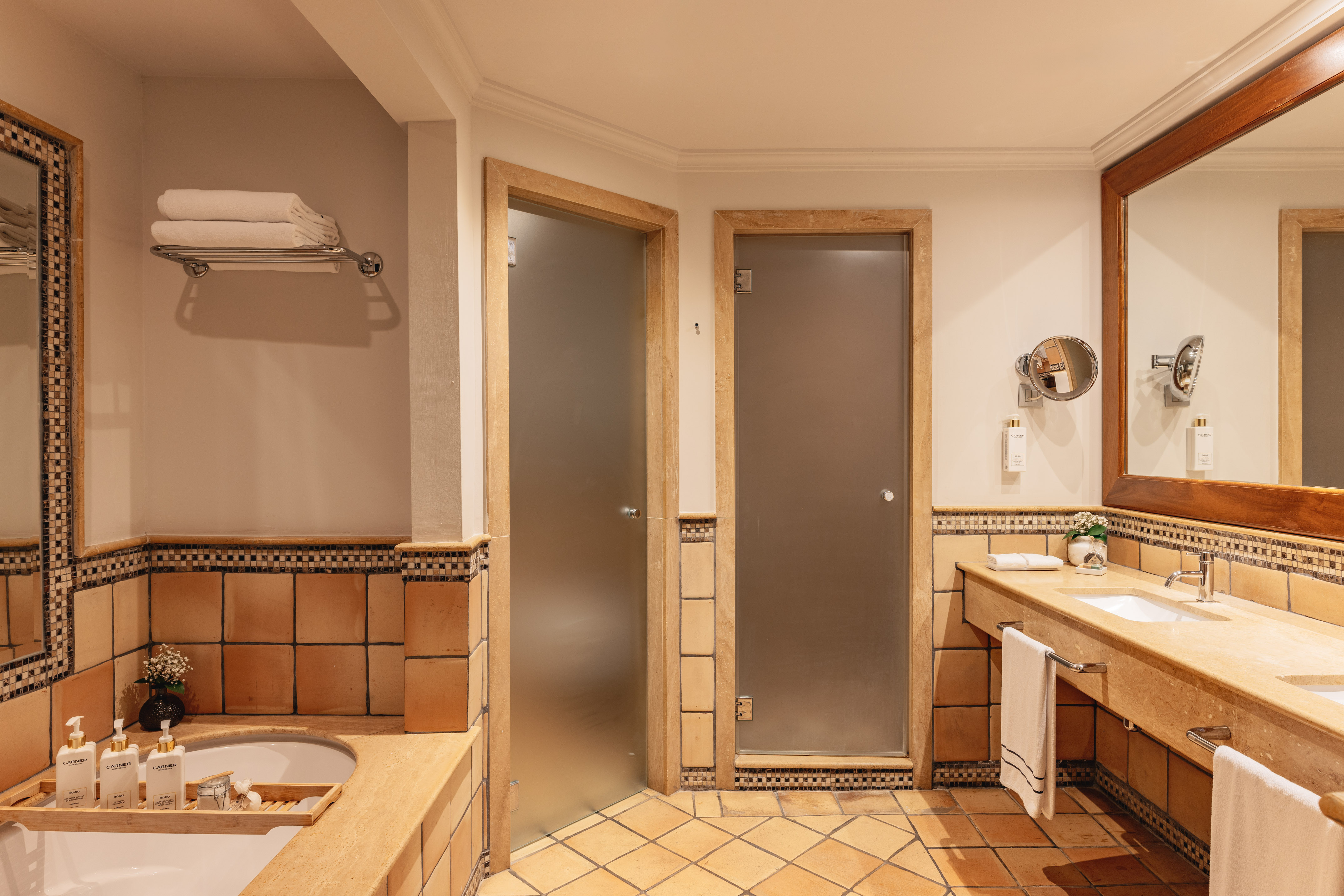 Hotel bathroom with terracotta tiles, double vanity, bathtub, and frosted glass doors.