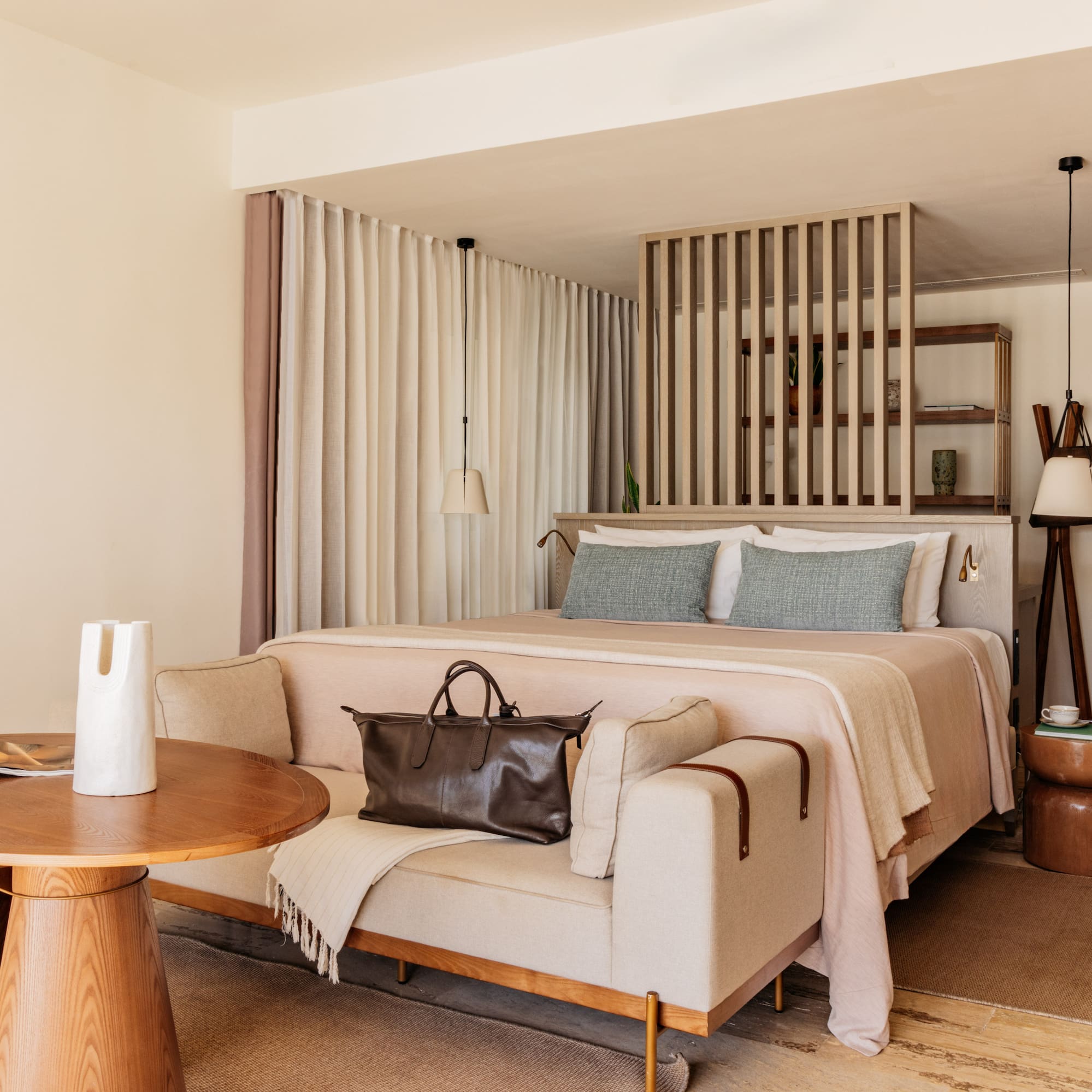 Modern hotel bedroom with king bed, light sofa, wooden accents, and neutral decor.