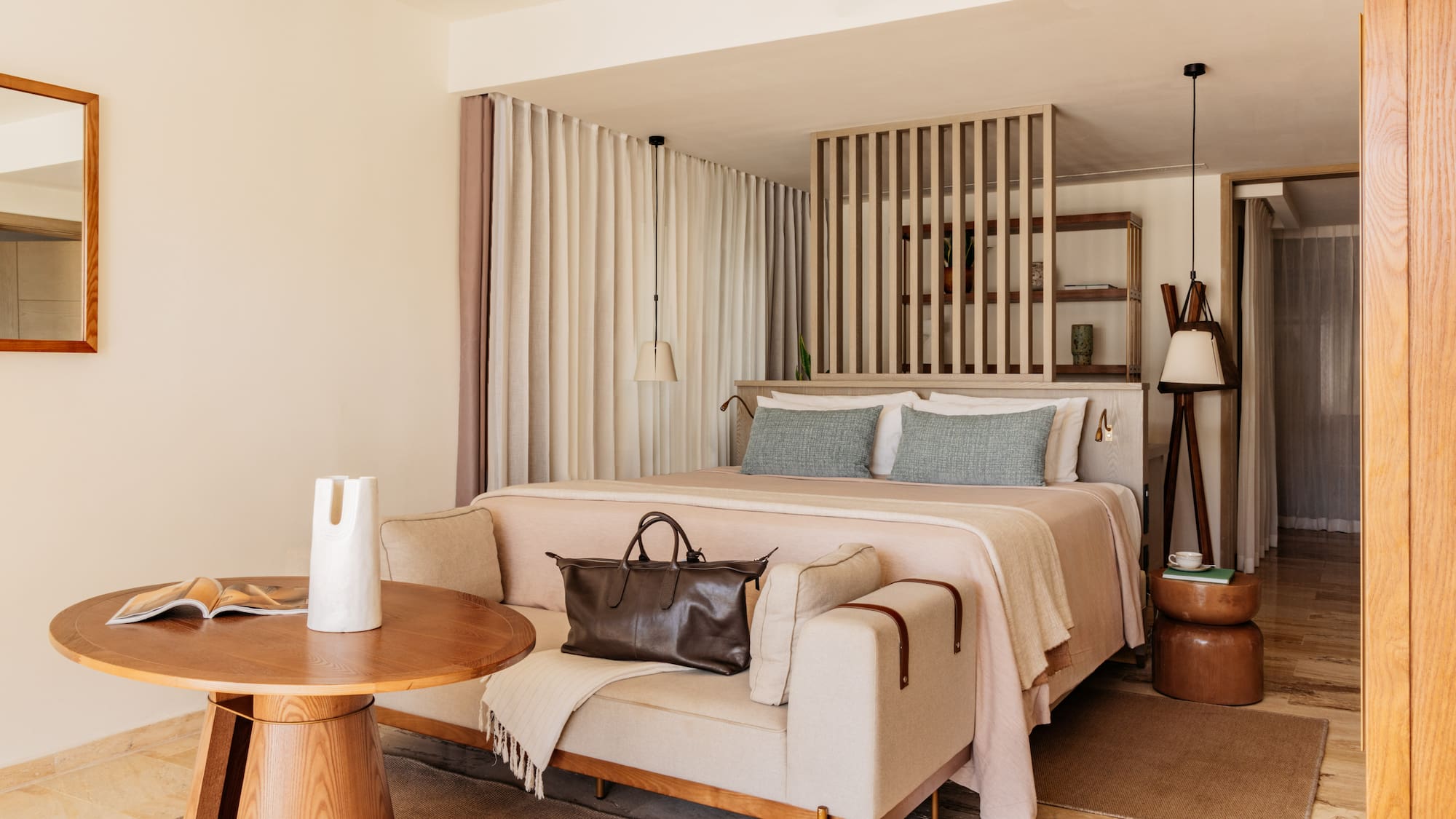 Modern hotel bedroom with king bed, light sofa, wooden accents, and neutral decor.