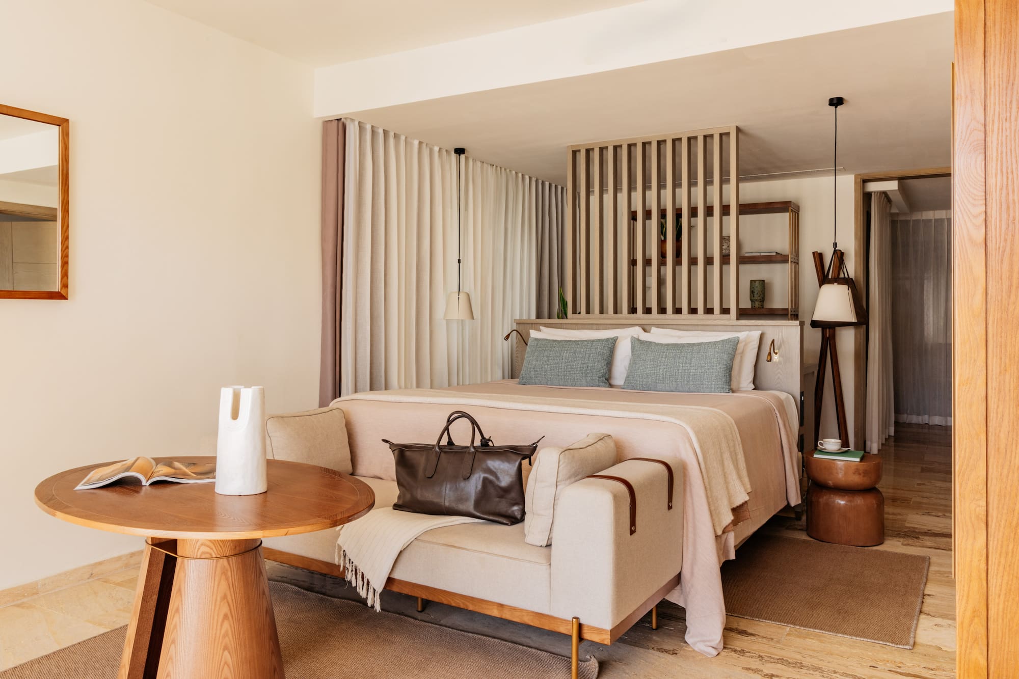 Modern hotel bedroom with king bed, light sofa, wooden accents, and neutral decor.