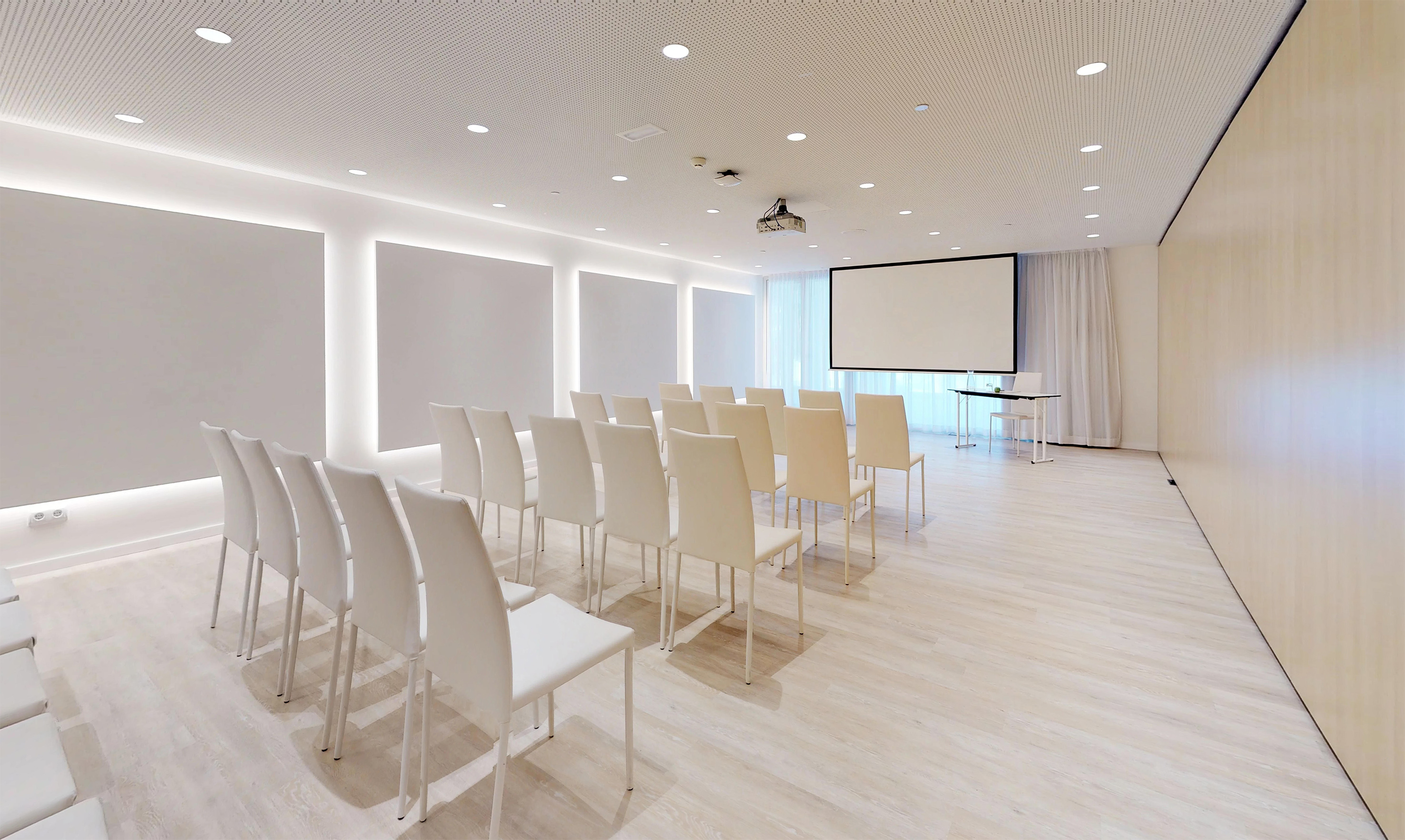 Modern conference room with white chairs, projector screen, and light wood flooring.