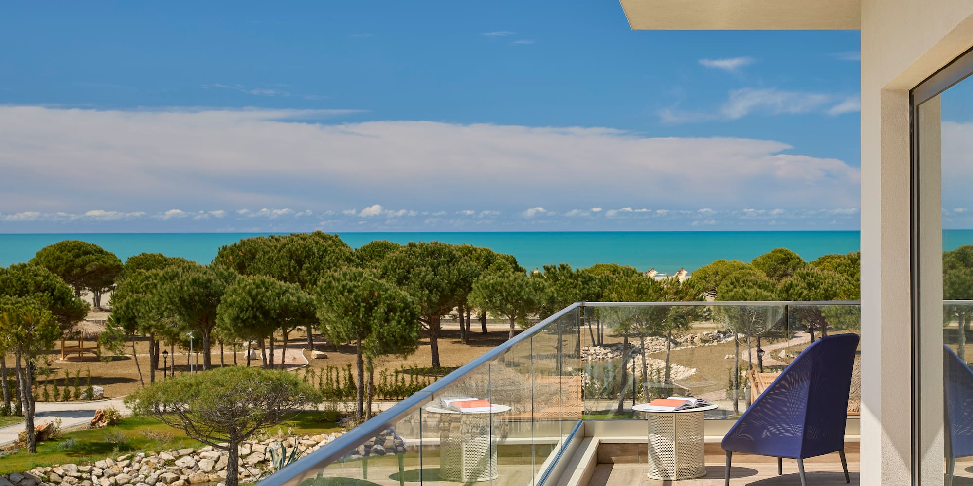 a deck with a chair and a glass railing overlooking a beach