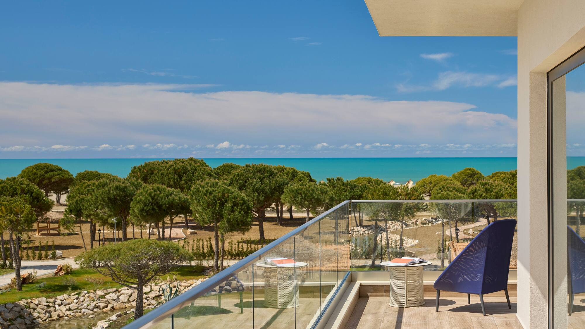 a deck with a chair and a glass railing overlooking a beach
