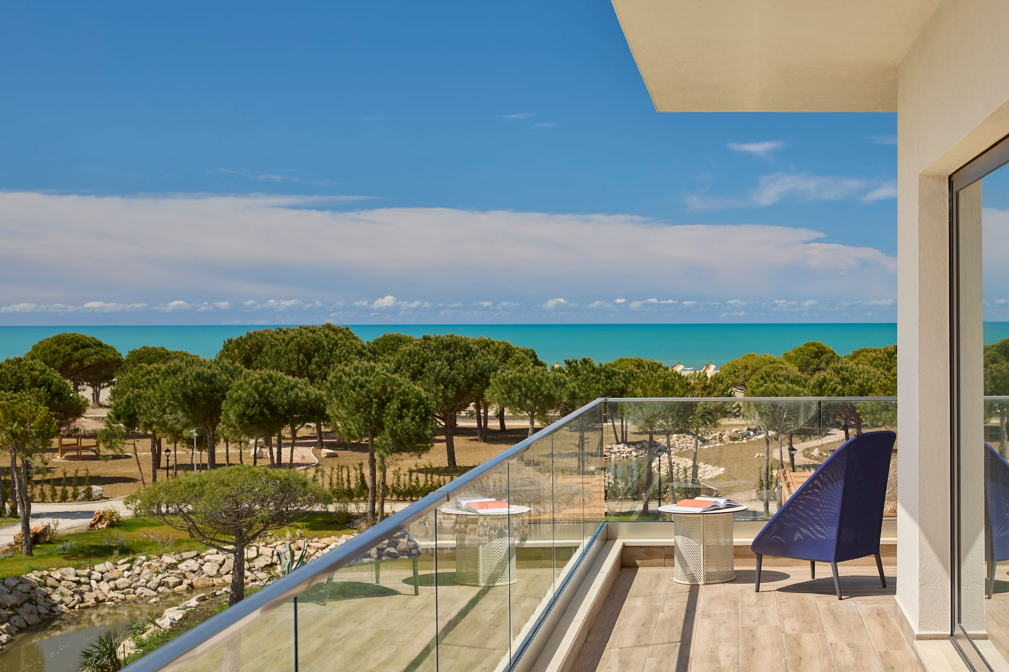 a deck with a chair and a glass railing overlooking a beach
