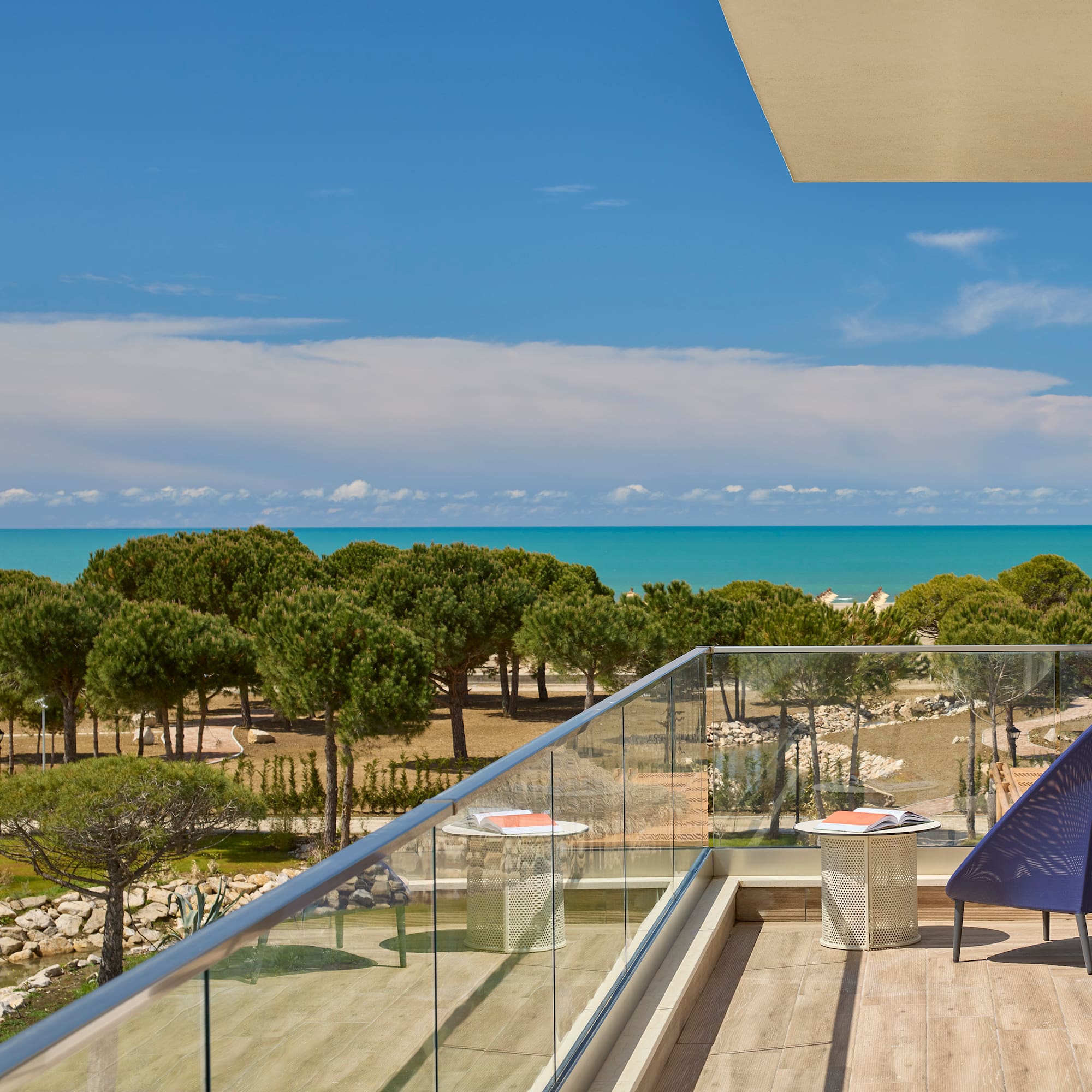 a deck with a chair and a glass railing overlooking a beach