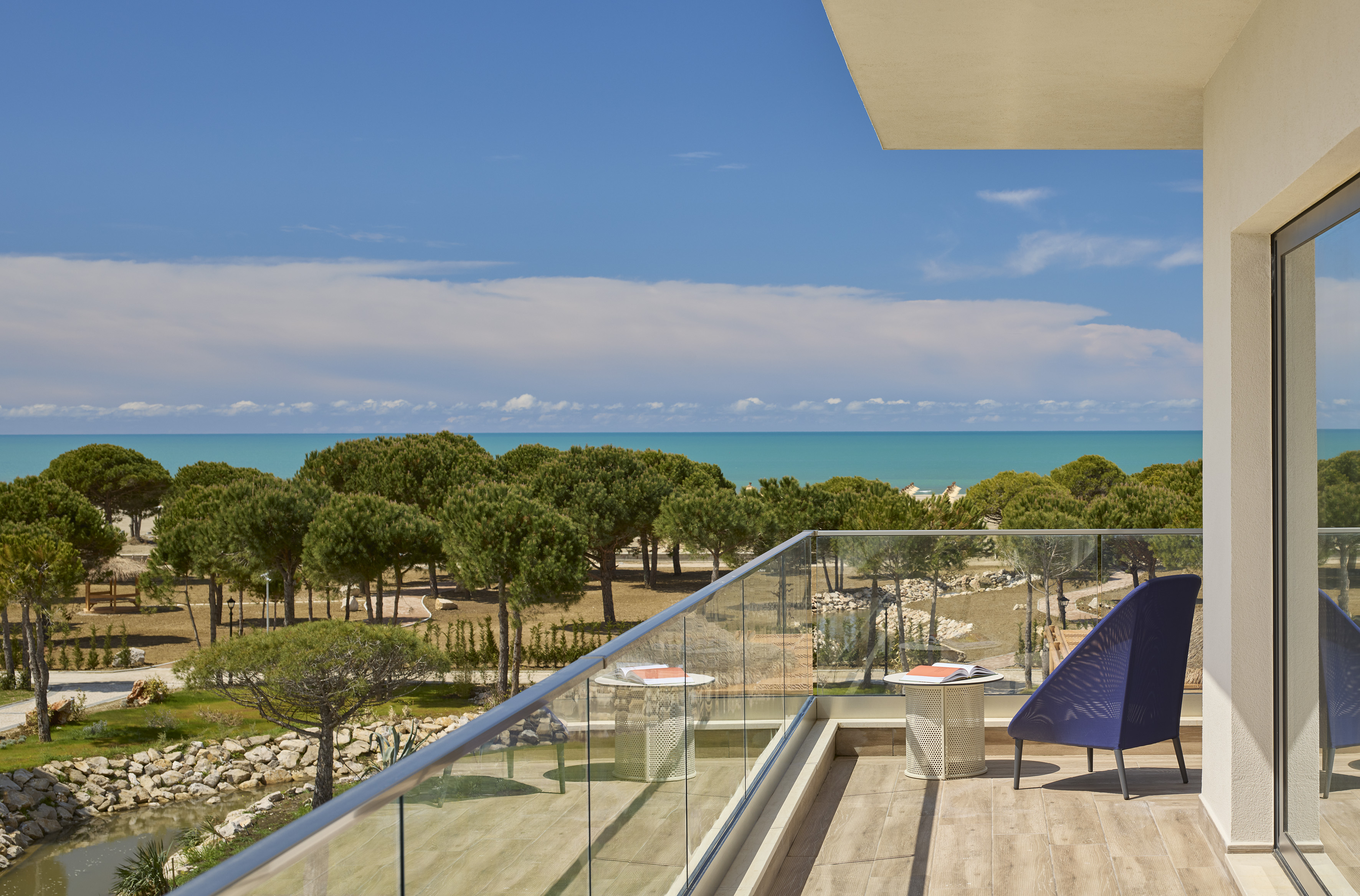 Balcony with turquoise ocean view, green pine trees, and clear blue sky.