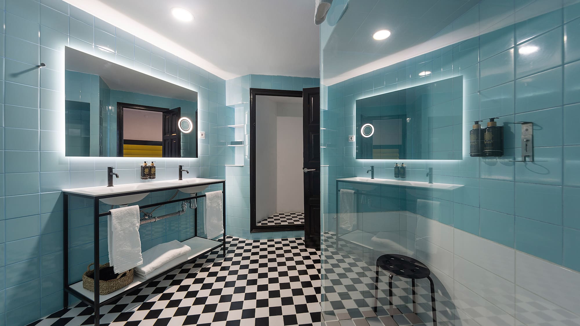 Modern blue bathroom with checkered floor, double vanity, backlit mirrors.